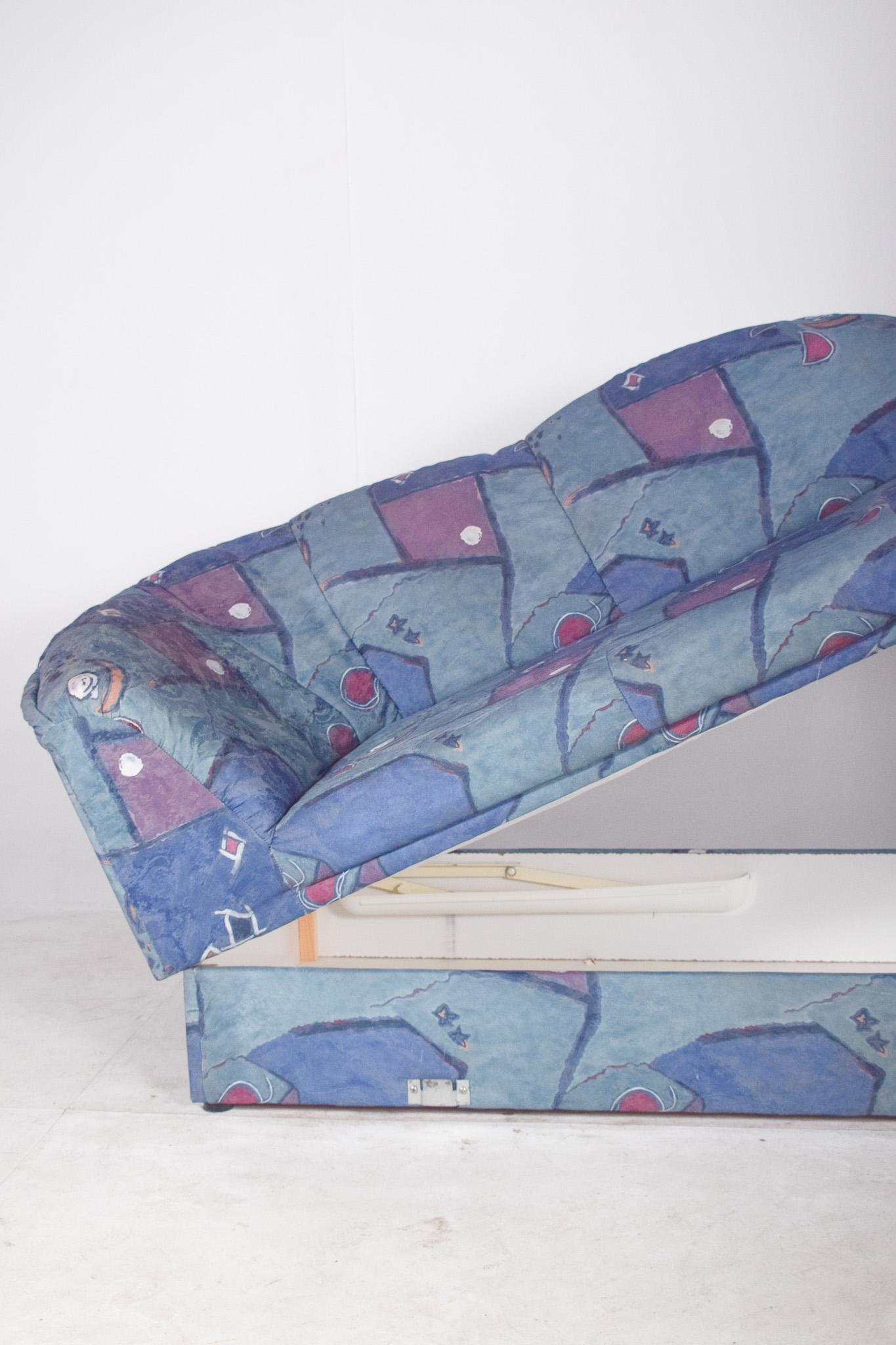 Upholstered sofa in shades of blue and purple. The curved, padded structure provides comfort and a relaxed look, ideal for living or relaxing areas. The fabric upholstery printed with abstract geometric shapes in shades of blue, purple and burgundy