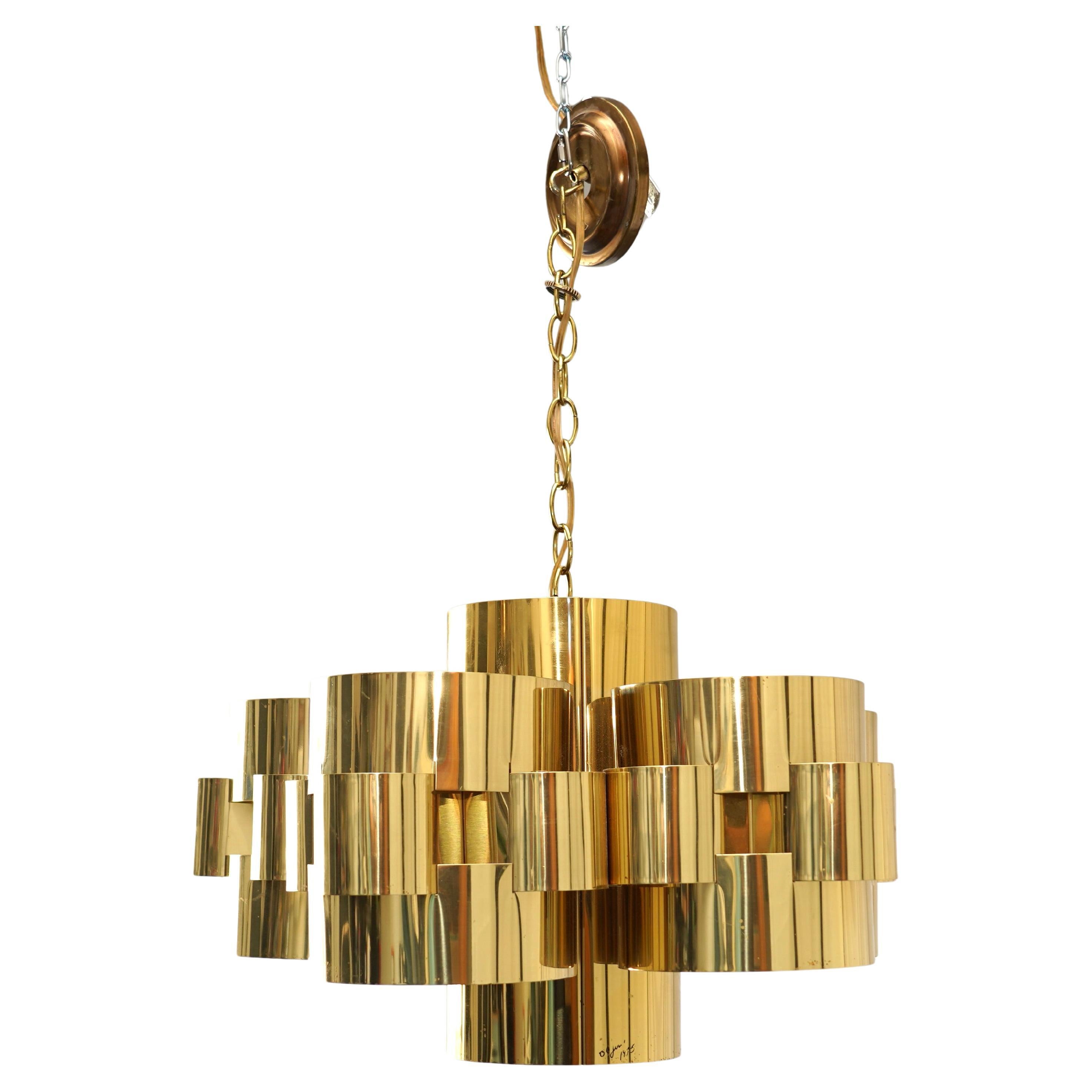 Stunning Sculptural brass chandelier by C. Jere, signed and dated 1975. Features a dramatic layered design of interlocking cylindrical brass forms that create stunning light reflections. A standout example of mid-century American studio design with