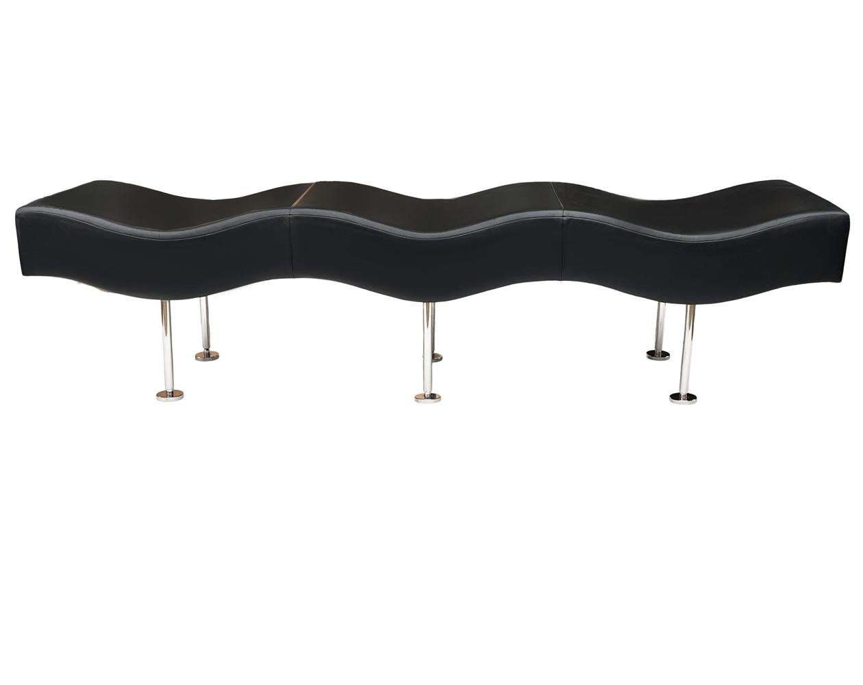 An extra long contemporary design produced by Brueton in the 1990's. It consists of a wavy design, black leather upholstery, and stainless steel legs. Leather has some small cuts and edge wear, so recovering is recommended.