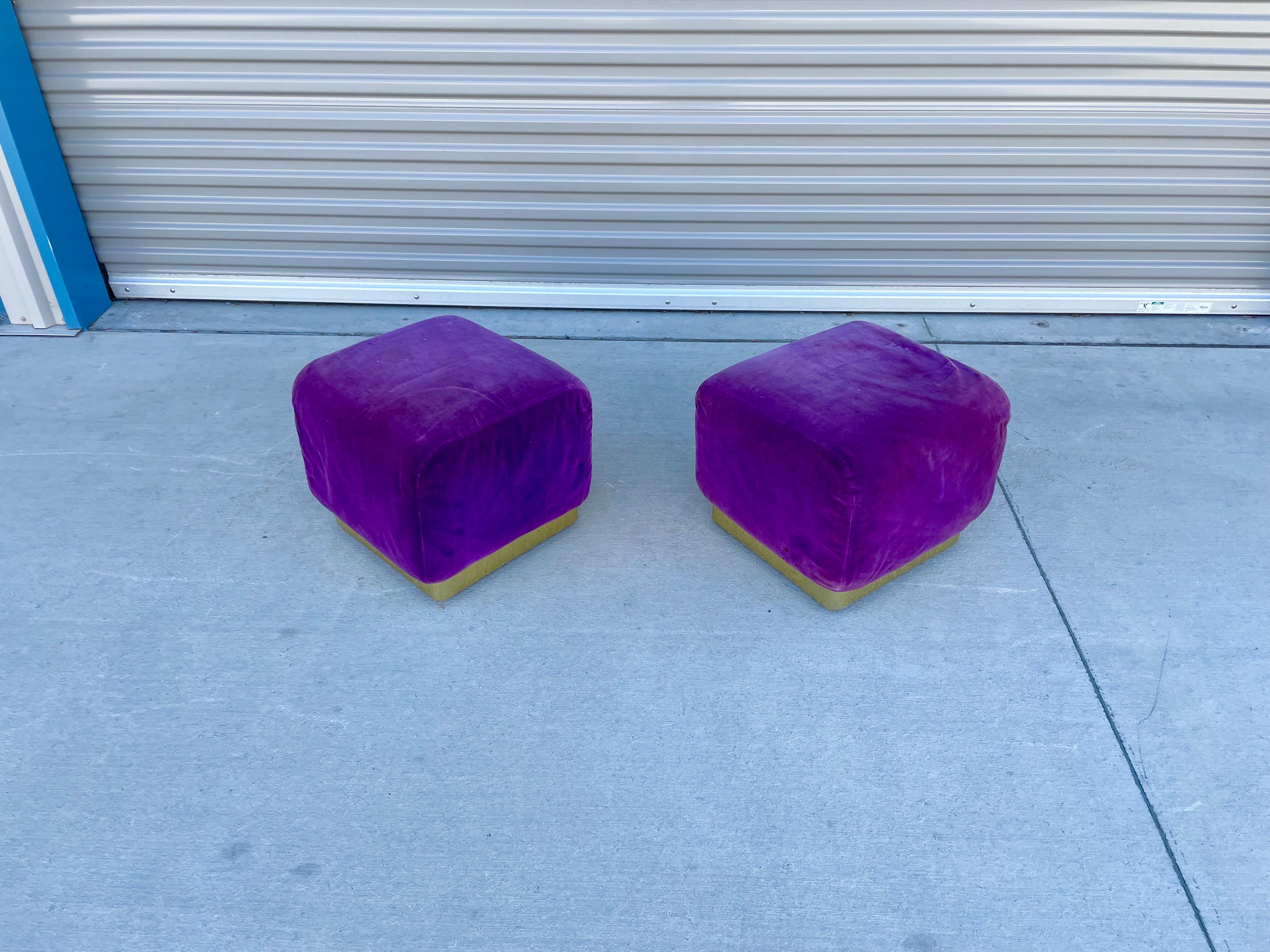 Midcentury pair of square shape brass ottomans. This pair of ottomans features a square shape design making them comfortable with a brass base, making them sturdy. The upholstery does need to be reupholstered, letting you make them the perfect