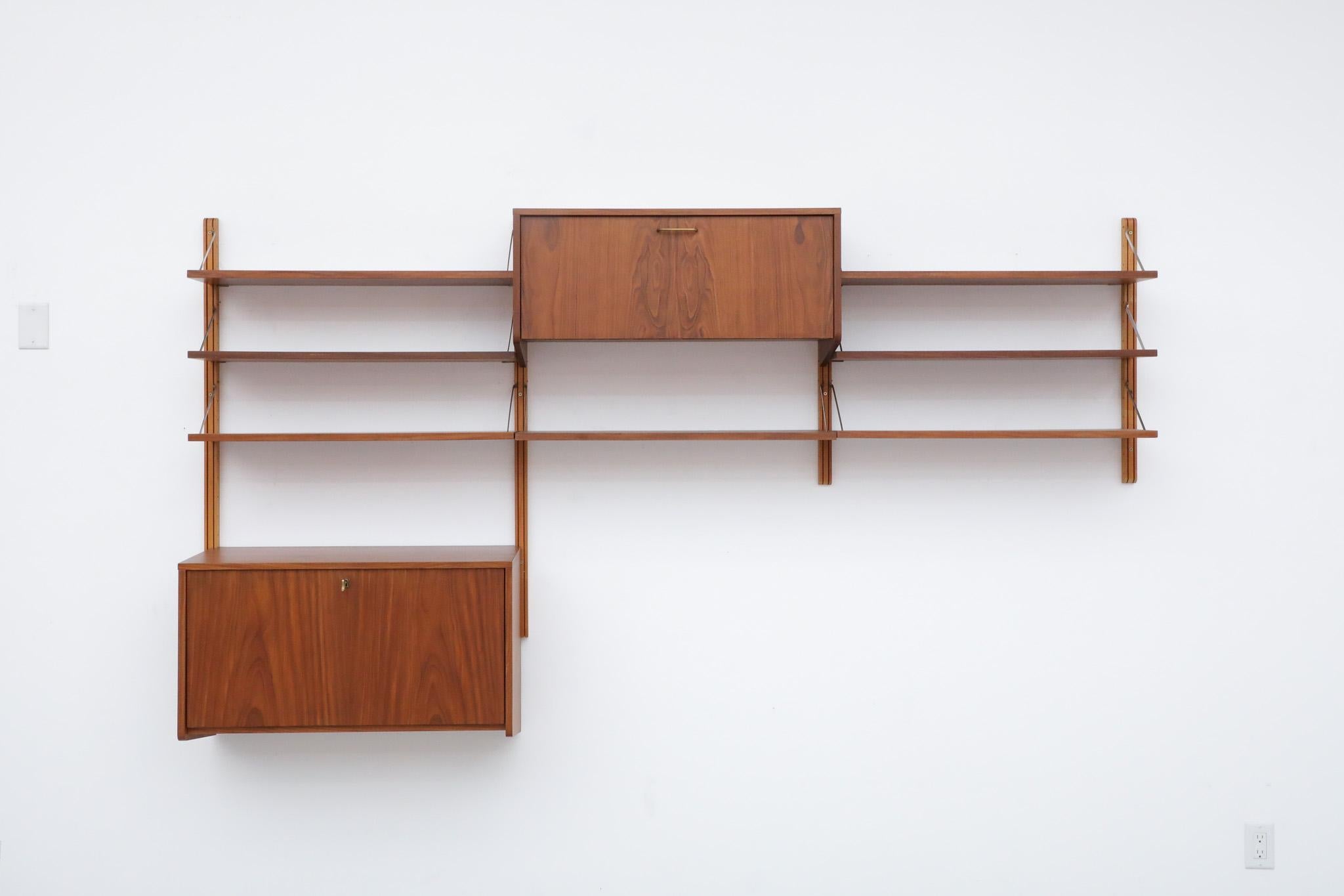 Stunning, Mid-Century, Poul Cadovius inspired teak wall mounted shelving system with attractive, brass risers and adjustable cabinets and shelves. A beautiful example of classic Mid-Century esthetics. The unit is in original condition with one