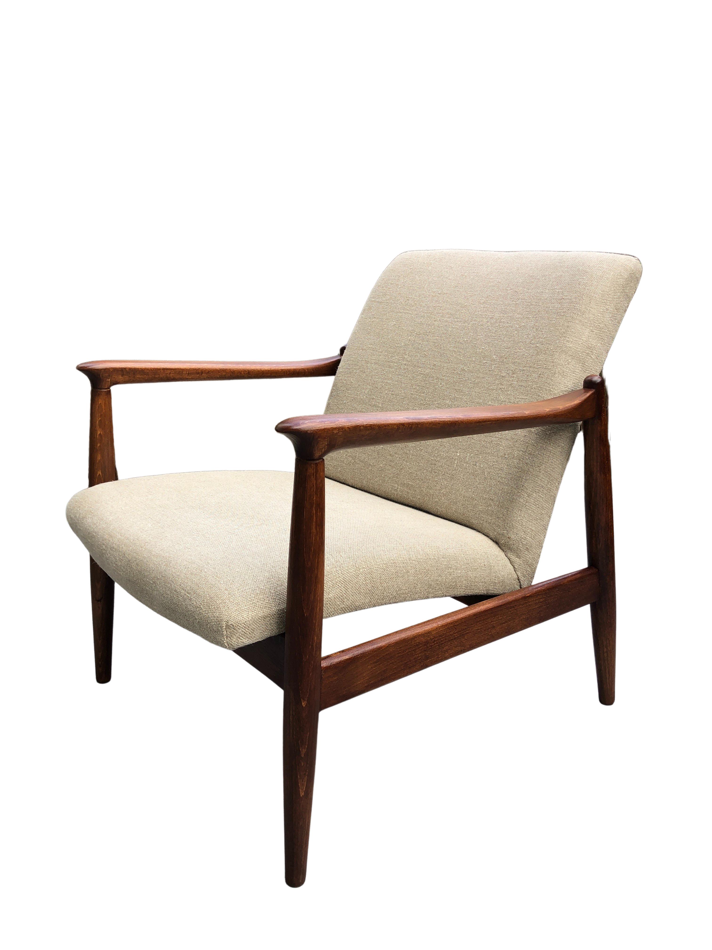 One of the icon of Polish mid-century design model GFM-64 armchair, designed by Edmund Homa, manufactured by Goscinska Furniture Factory in Poland in the 1960s. 
The structure is made of solid beechwood in a warm wallnut color, finished with a semi