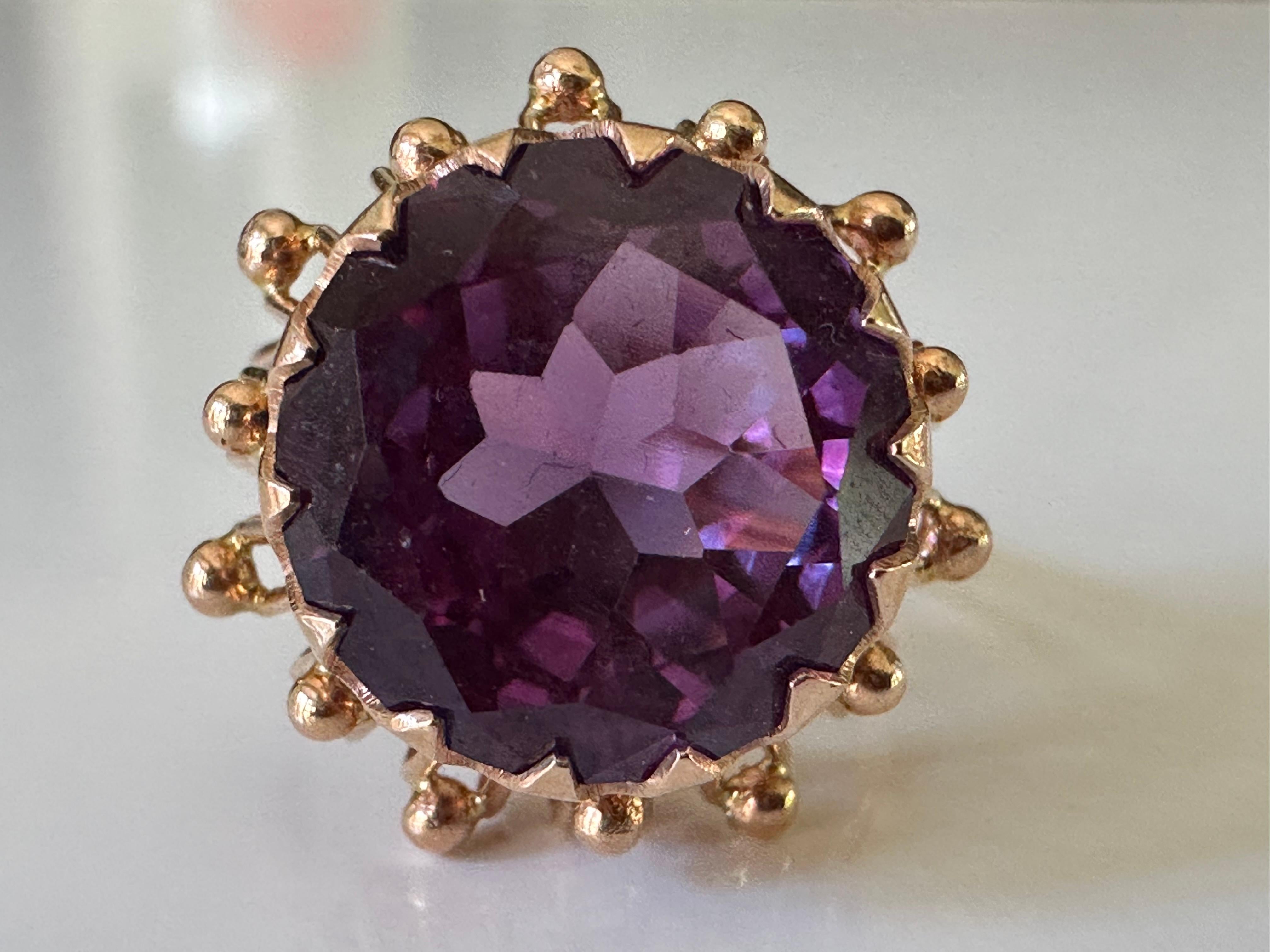 Crafted in the 1950s, this mid-century cocktail ring features a round purple synthetic sapphire set in 14K yellow gold with delicate piercing. 

