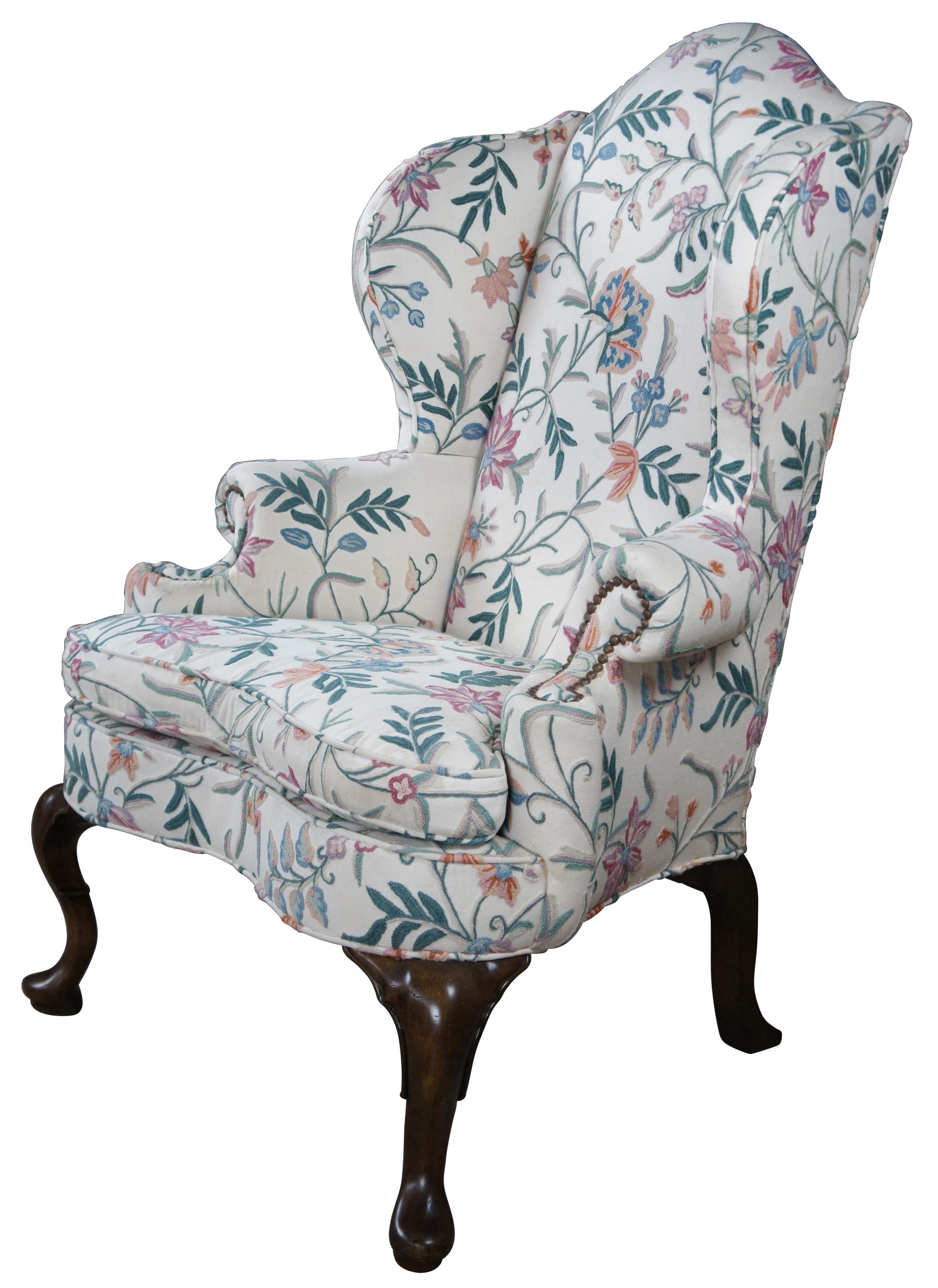 Mid century oversized Queen Anne wingback chair. Made of mahogany with a wide stance, accented with rolled arms, camel back top and scrolled legs. Upholstered in a beautiful floral crewel fabric. 
 