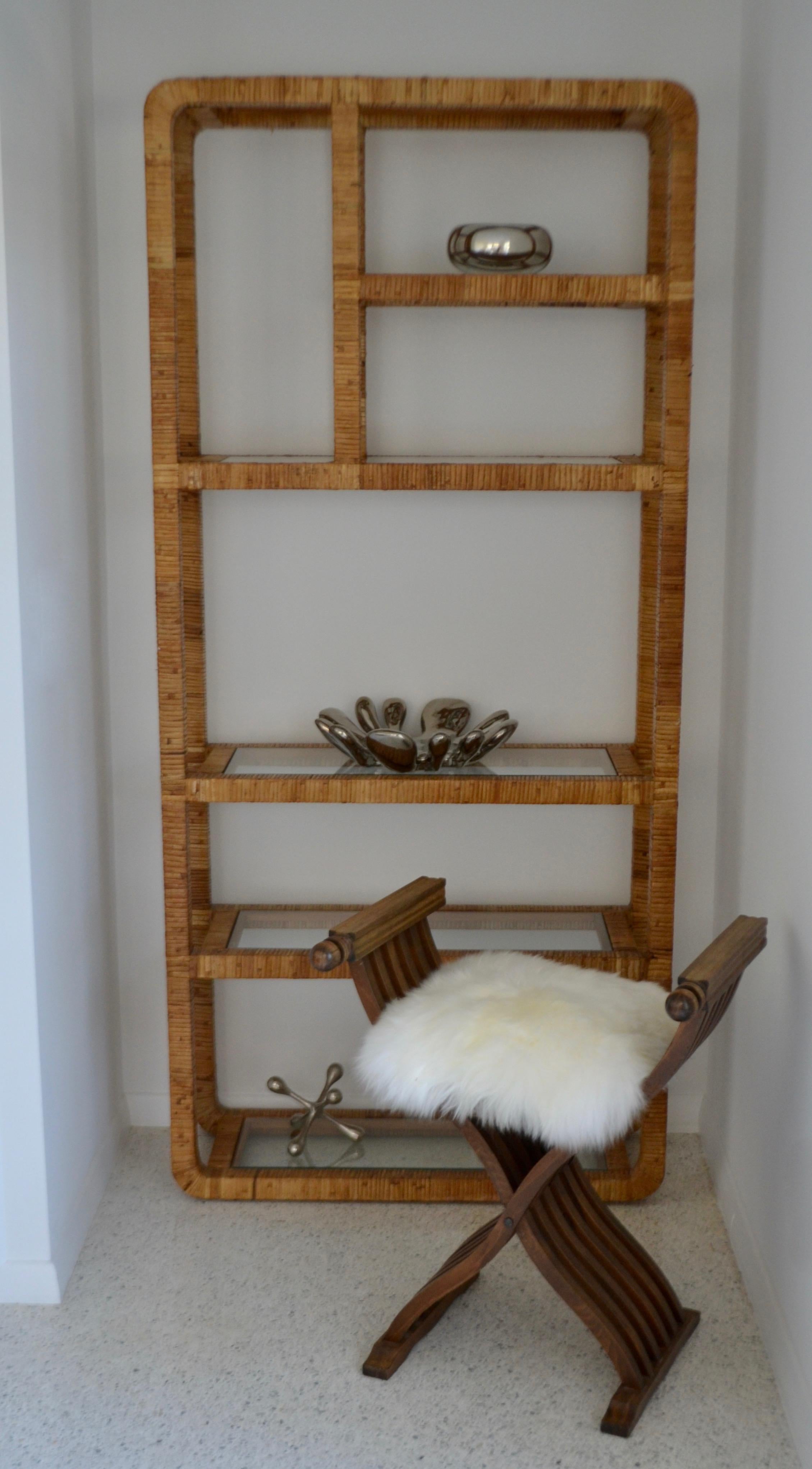 Striking midcentury rattan étagère, circa 1960s-1970s. This sculpturally designed rattan wrapped hardwood bookcase or bookshelf is accented with inset glass shelves.