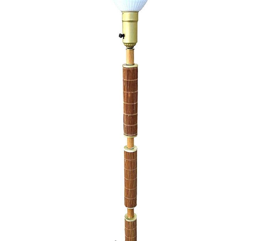 Questa lampada a palo in rattan di metà secolo ispirata a Paul Frankl, splendidamente restaurata, presenta un unico palo in rattan centrato con 3 sezioni avvolte in ottone e sezioni in rattan di canna e una base scolpita in mogano biondo. La lampada
