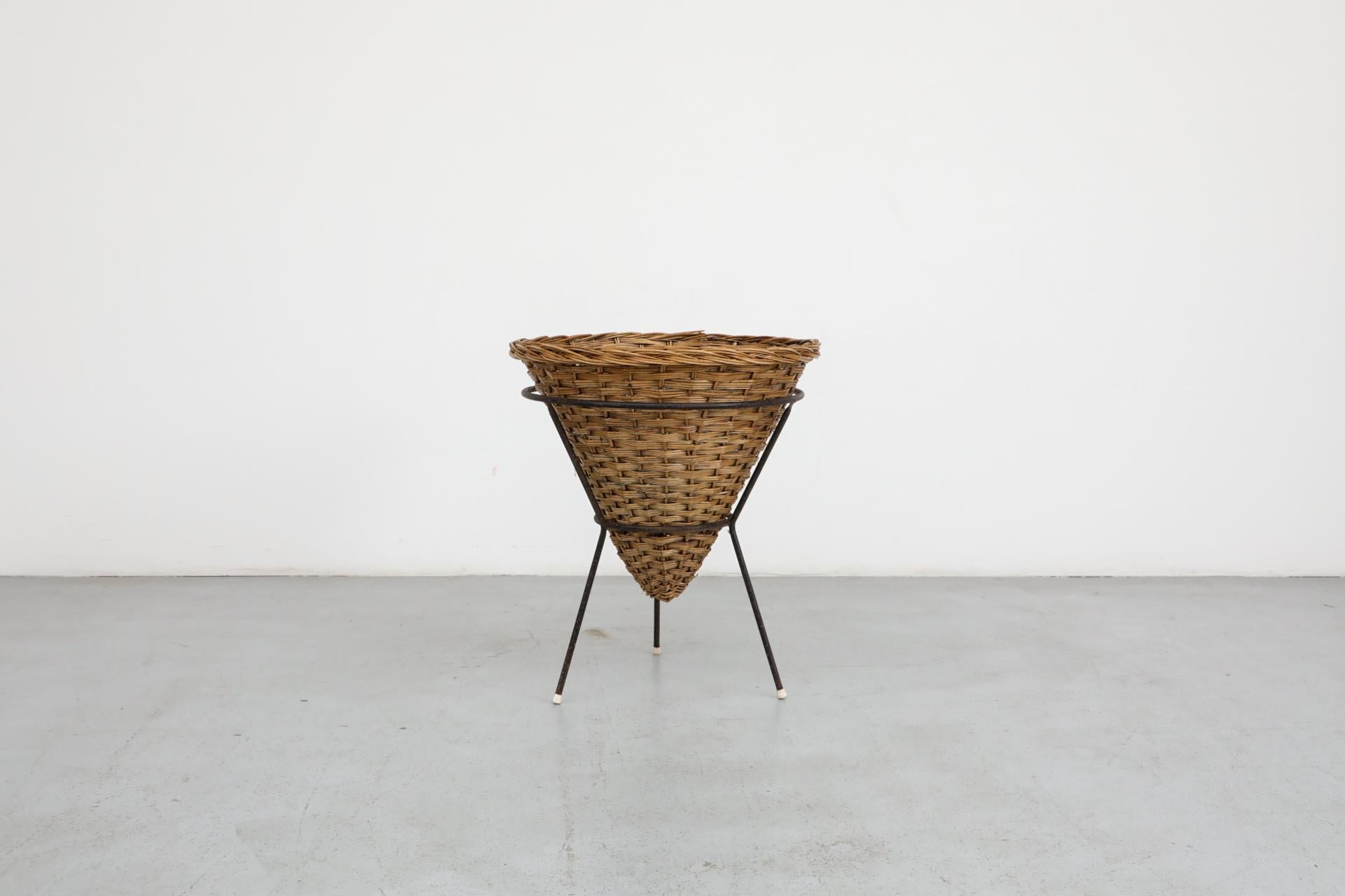 Cestino in rattan intrecciato di metà secolo con colore blu sbiadito all'interno del cestino e telaio a treppiede smaltato nero. Ottimo per coperte, riviste, piante o biancheria. In condizioni originali, con usura visibile, compresa una possibile