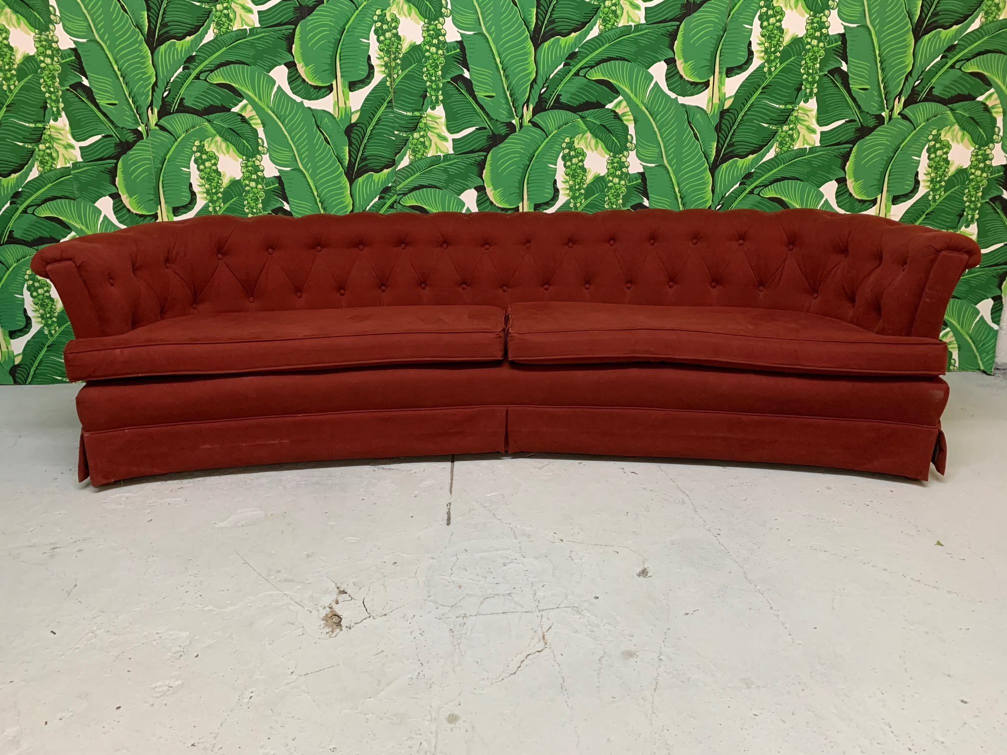 Large mid-century tufted sofa in the manner of Dorothy Draper features a curved shape and deep rich red velvet type upholstery.  Very good condition with no tears or holes and only very minor imperfections consistent with age.