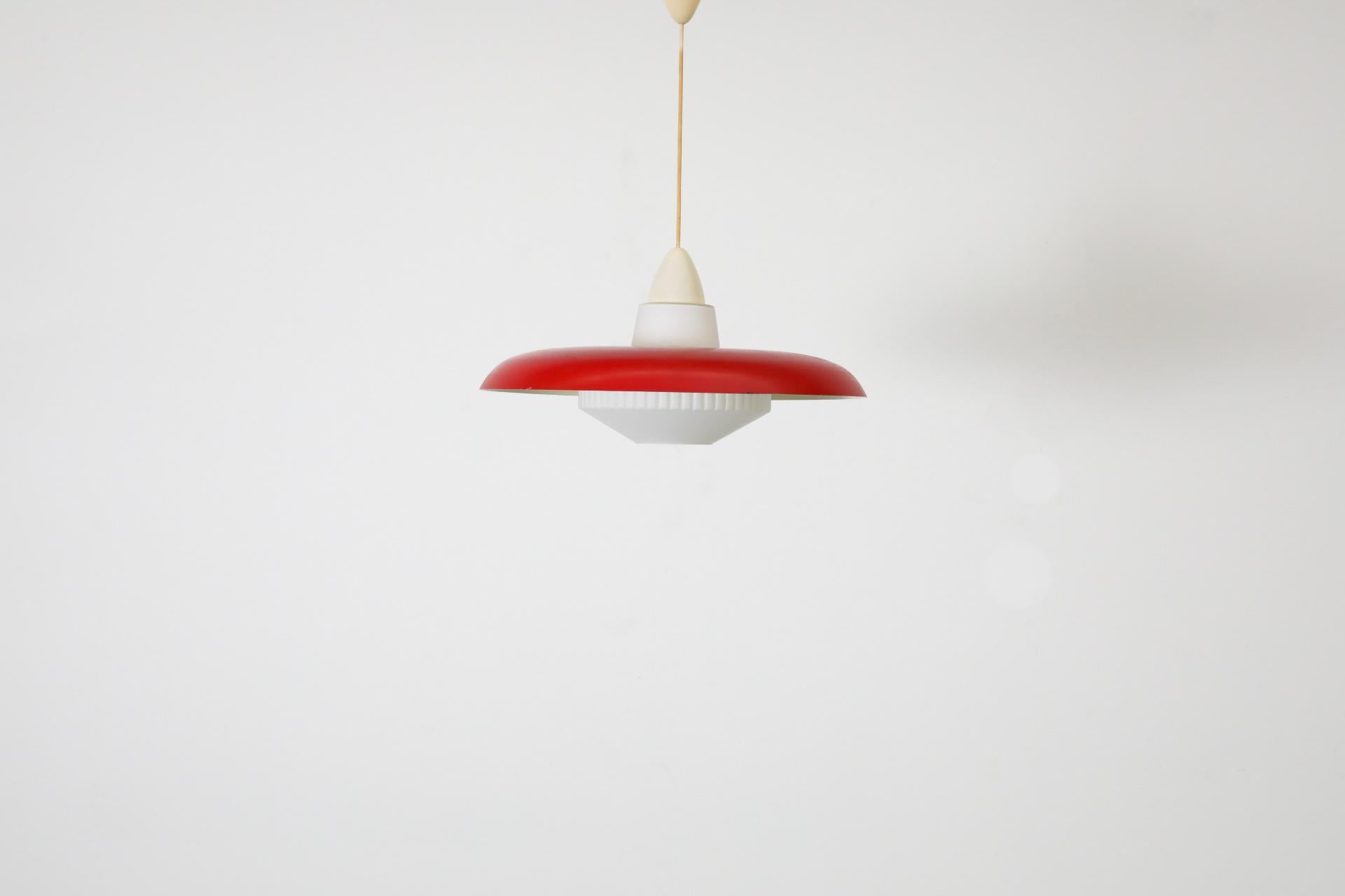 Rare suspension de plafond Philips avec abat-jour décoratif en verre au lait et dôme en métal émaillé rouge. L'abat-jour en verre au lait est orné d'une bande décorative nervurée. L'abat-jour en métal émaillé rouge repose sur la forme en verre de