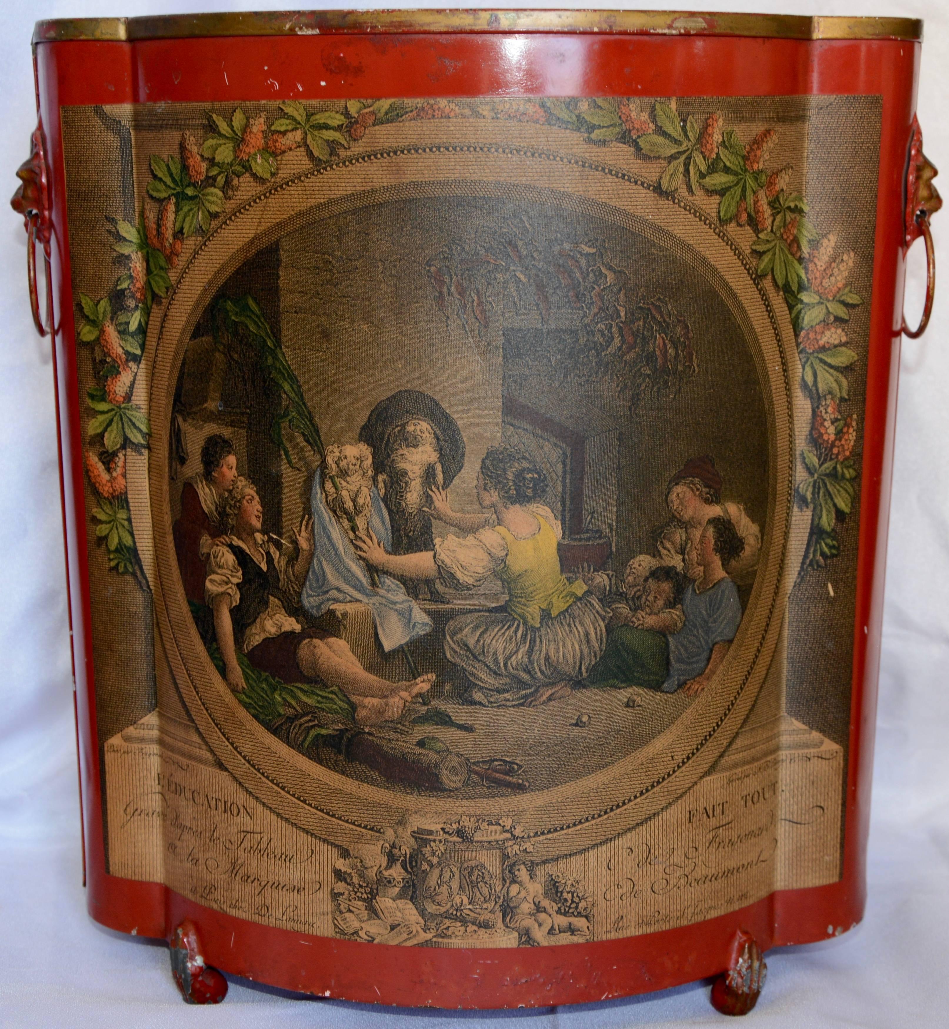 A vibrant red adorns this midcentury tin waste basket. It is embellished with a decoupage print depicting what appears to be a family with their dogs. The scene is edged with a floral border. The pair of handles are of lions heads with the loops in
