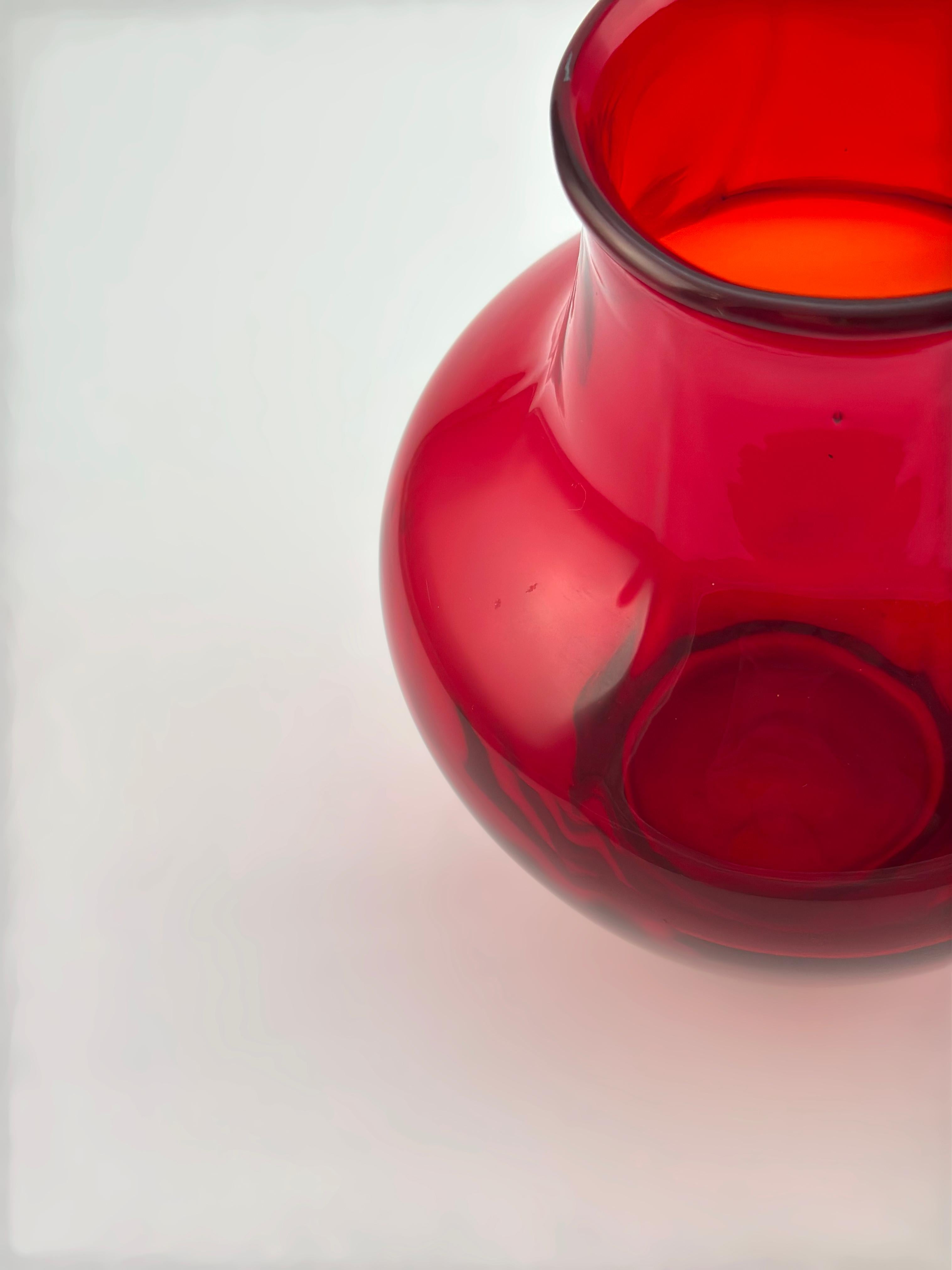 Diese rubinrote Glasvase ist eine seltene Variante des britischen Kunstglases aus der Mitte des Jahrhunderts und wurde von Whitefriars Glass, England, um 1950 hergestellt. 

Das aus dem für sie typischen tiefroten Glas geblasene Stück wird als