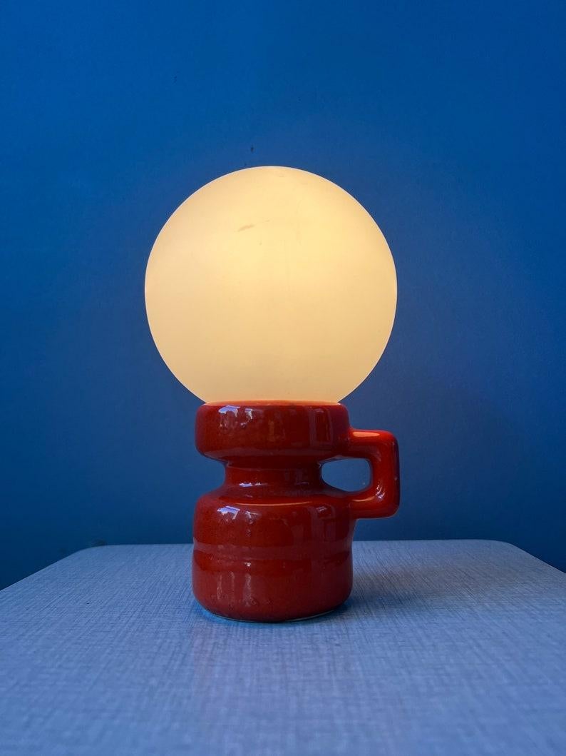 Petite lampe de table en céramique rouge d'Allemagne de l'Ouest avec abat-jour en verre opalin. La lampe nécessite une ampoule E14 et dispose actuellement d'une fiche de connexion à l'UE.

Informations complémentaires :
MATERIAL : Céramique,