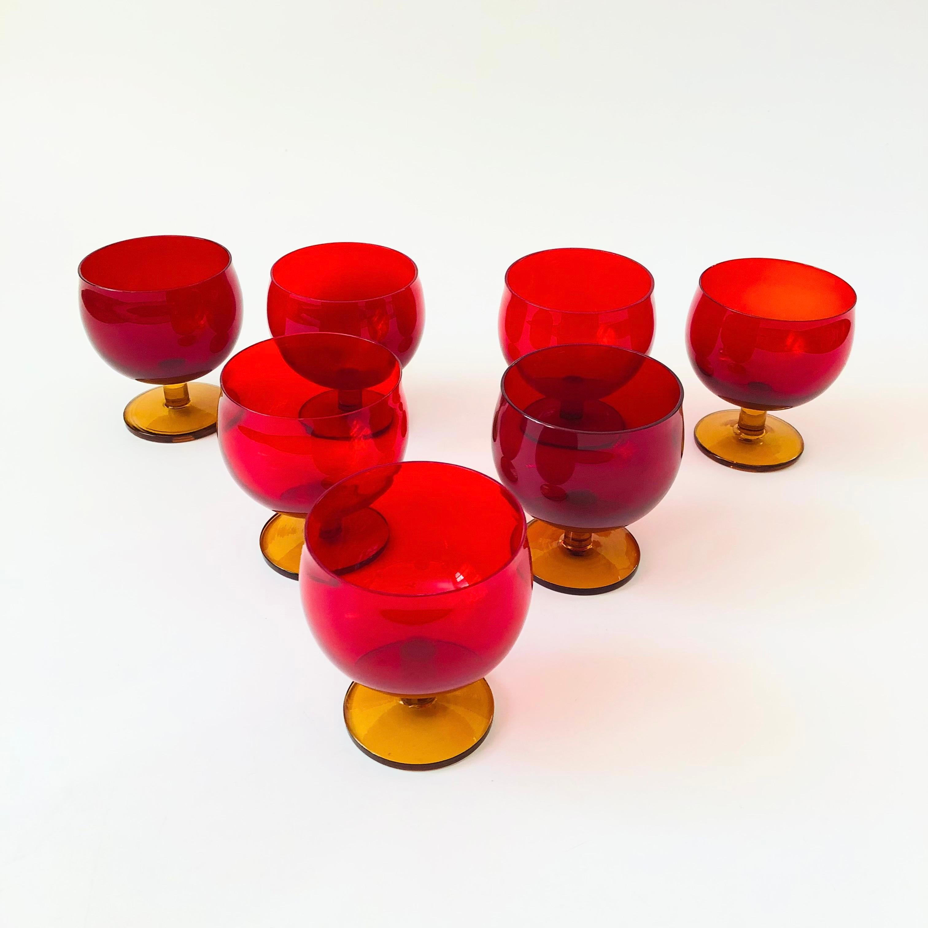 A set of 7 vibrant mid century wine glasses. Each with ruby red tops and amber stems. Subtle variation in the red hue of each glass. A beautiful and unique set.


