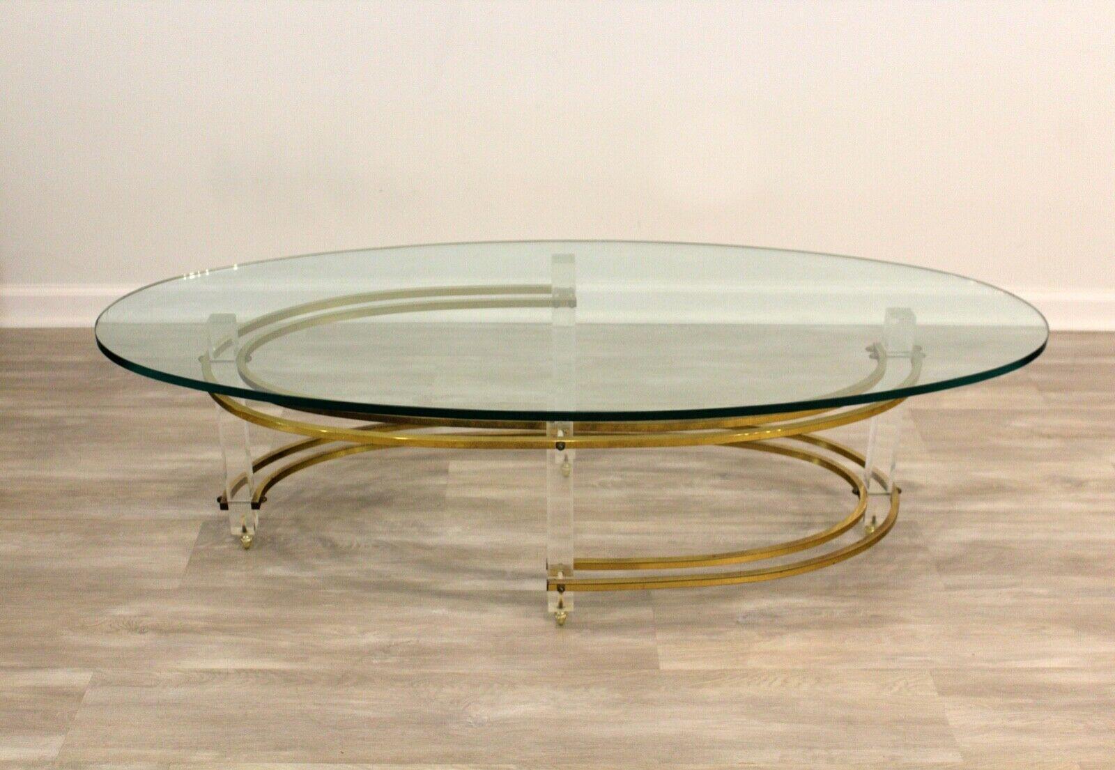 Lucite legs are adorned with brass acorn feet which support an oval glass top coffee table. Additional brass supports connect the legs adding a sophisticated material to this mid century and Hollywood Regency table.

Dimensions: 55.75 W x 23 D x