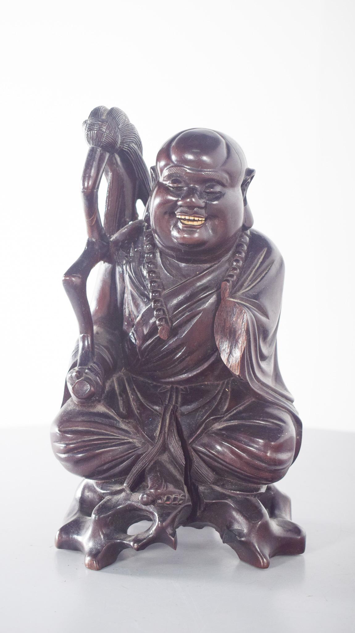 Scultura in resina di Budai. Con un'espressione gioviale e ridente, è seduto in posizione rilassata e indossa ampie vesti con drappeggi minuziosi e una collana di perline, simbolo di saggezza e spiritualità. Nella mano destra tiene un bastone con