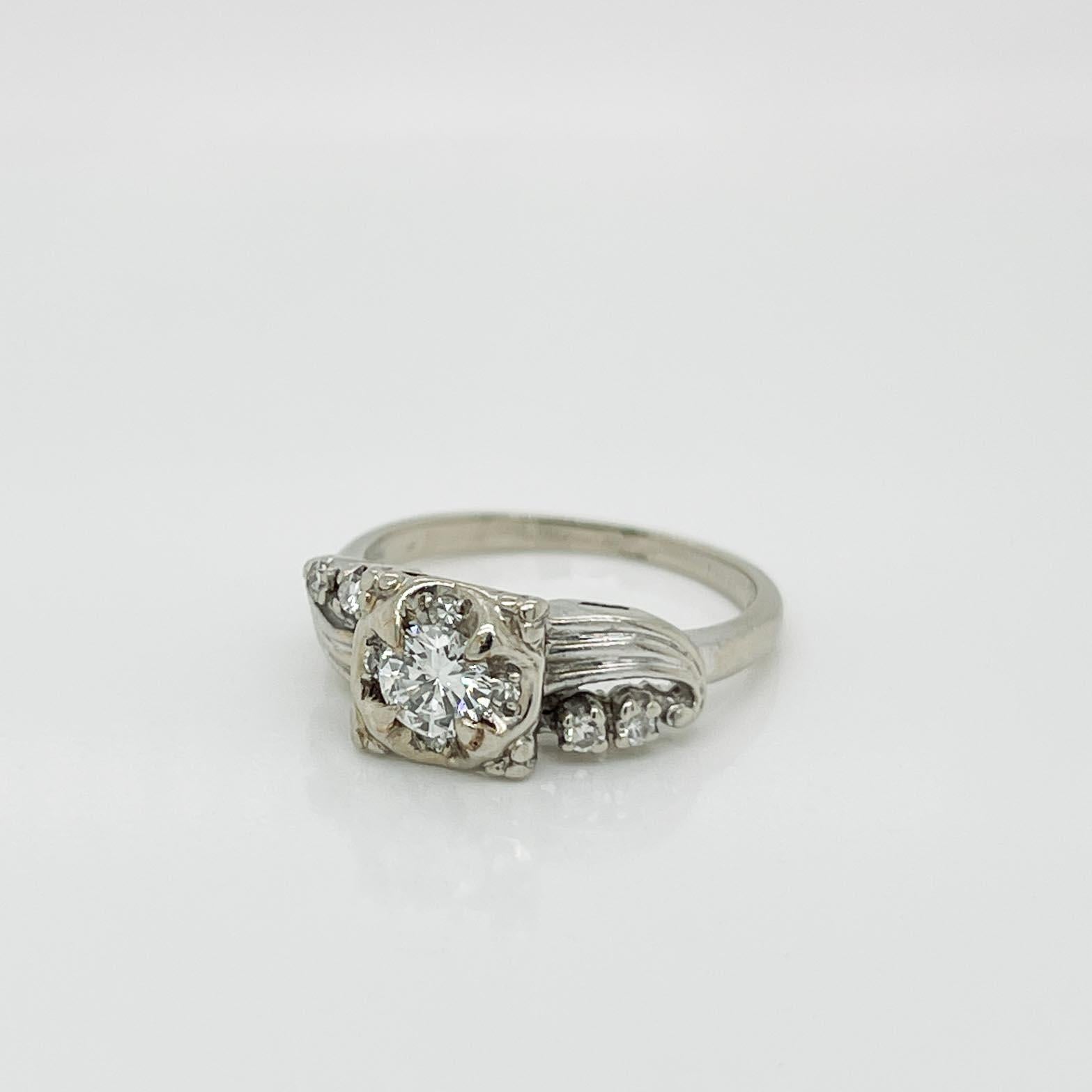 A fine Mid-Century gold & diamond engagement ring. 

In 14 karat white gold with a retro openwork design. 

Set with a round brilliant cut ca. 0.38 ct. white diamond prong set in the center of its S-curved setting and accented by 8 small round
