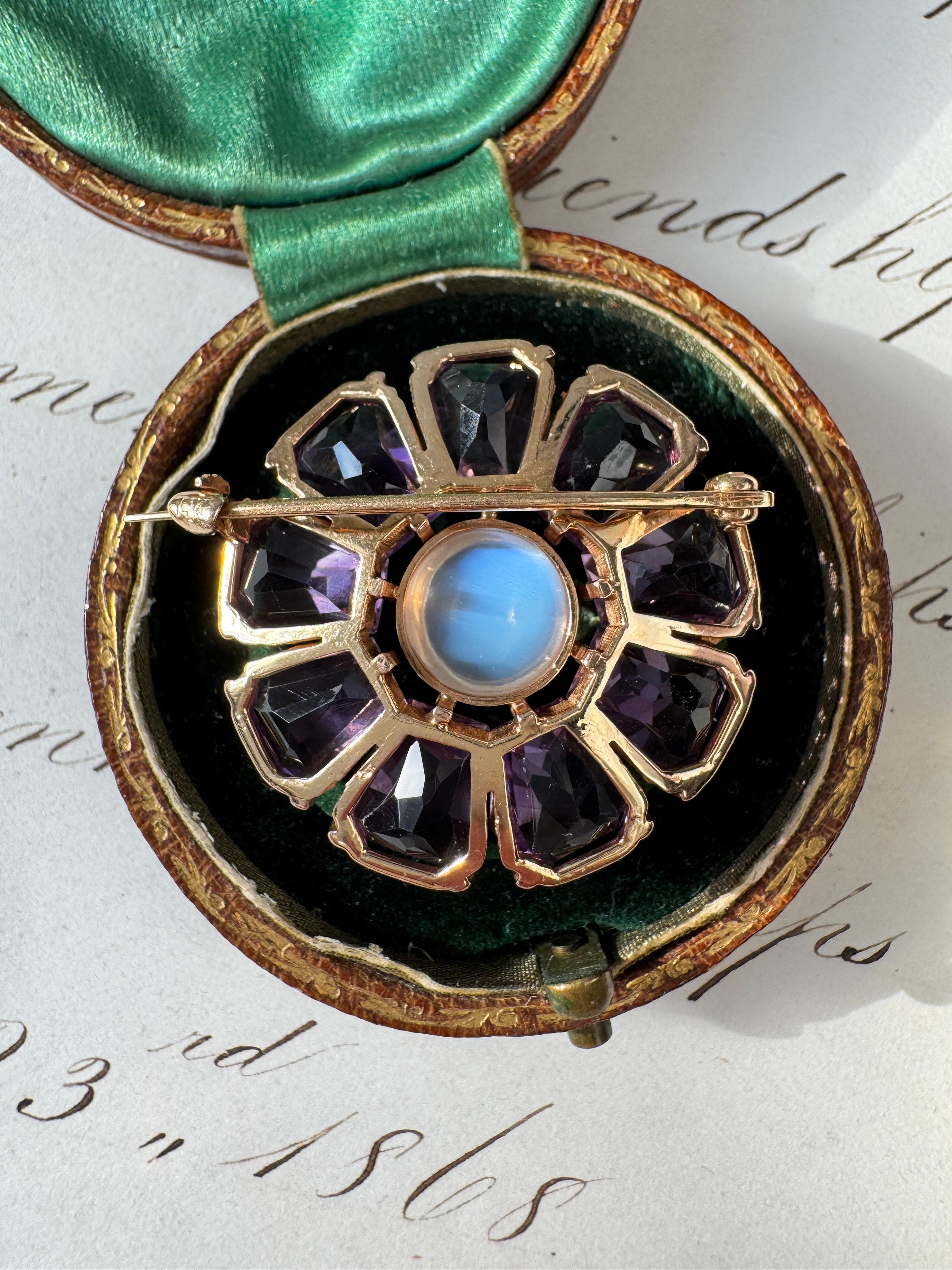 This charming mid-century floral brooch by Binder Brothers will add a touch of whimsy to any jewelry collection! At its heart, a dreamy cabochon moonstone shimmers with a mesmerizing blue sheen, while nine sparkling amethyst petals dance around it.