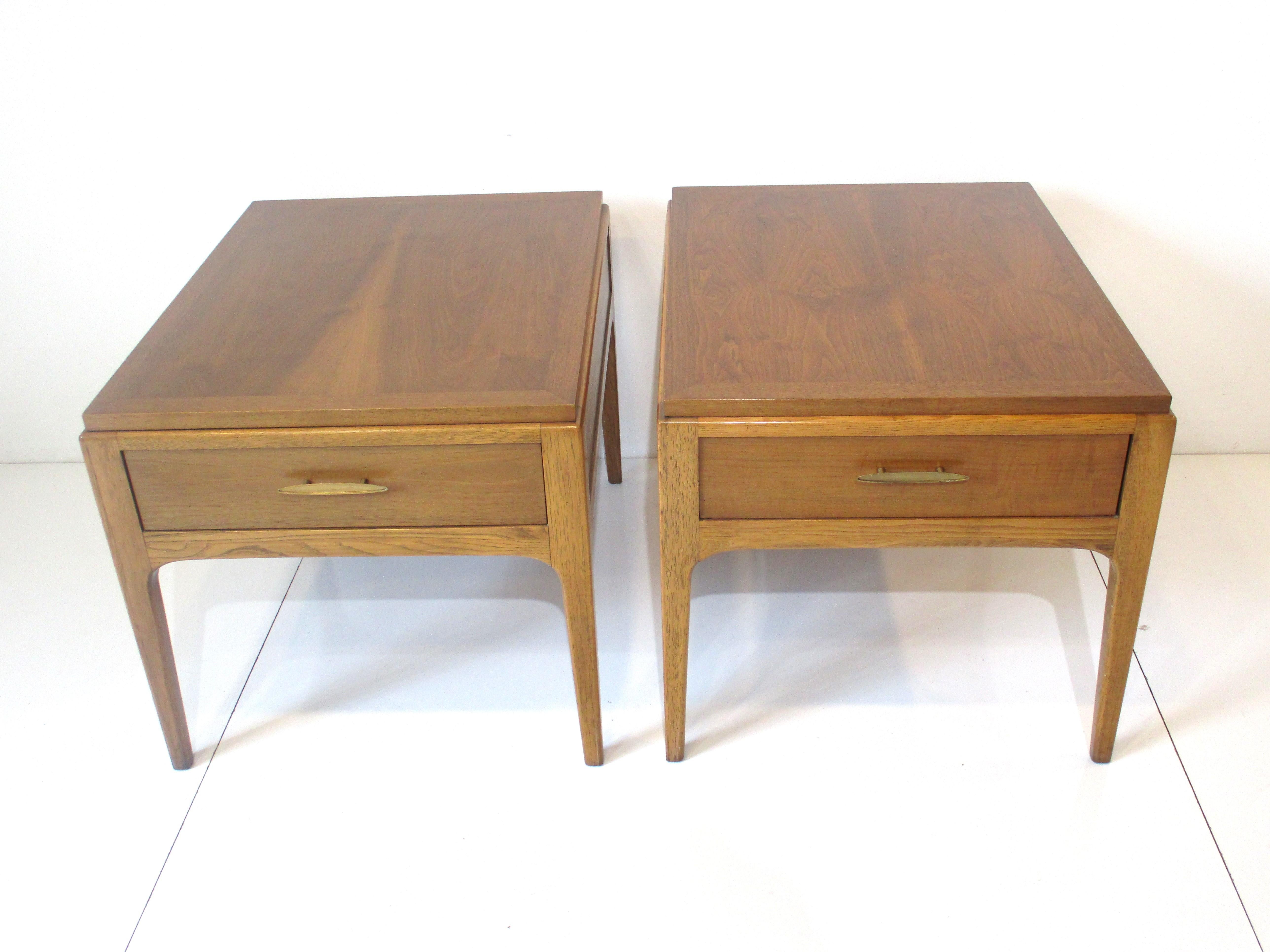 A pair of well crafted end tables with walnut tops and mahogany frames sitting on tapered legs each piece with a single drawer and bronze styled pulls. Manufactured and designed by Altivasta Lane from their Rhythm Collection.