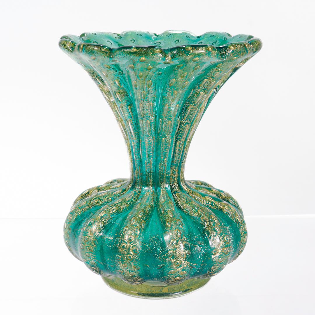 Vase en verre d'art de Murano datant du milieu du siècle dernier.

Par Barovier&Toso.

En forme de trompette Bullicante nervurée en verre vert avec des bulles capturées et des inclusions de paillettes d'or.

Soutenu par un pied en forme de