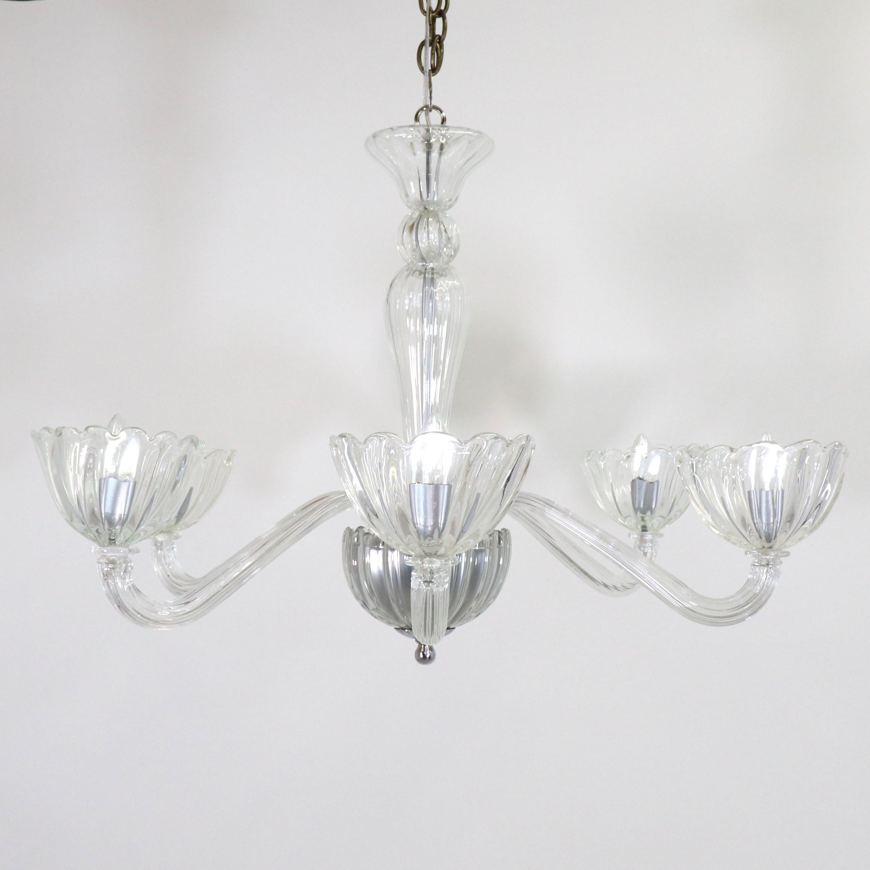 Experience the timeless elegance of this exquisite Murano chandelier. Featuring five gracefully scrolling arms adorned with scalloped cups and refined chrome details, this chandelier is crafted from pristine, colorless Venetian glass, casting a
