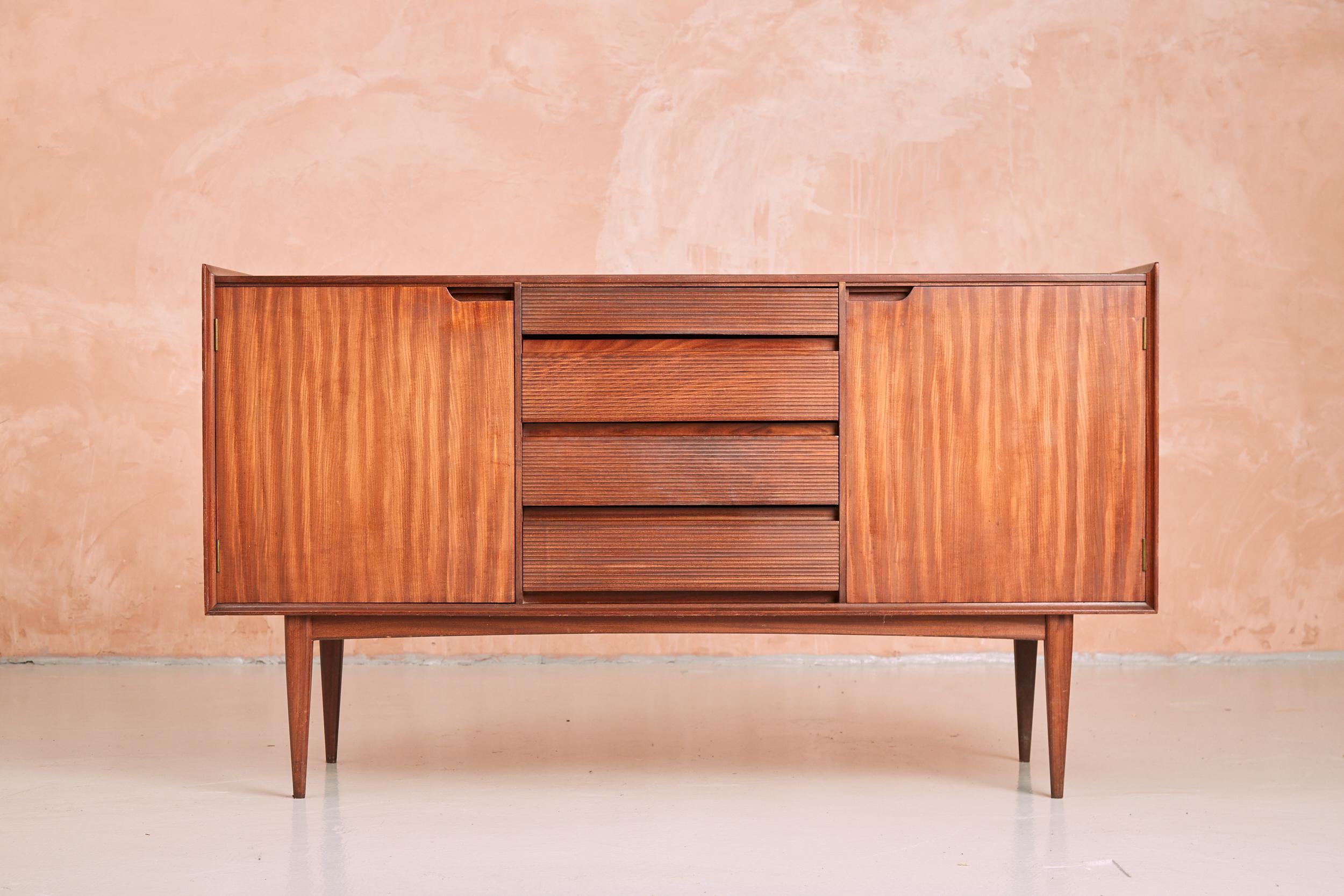 An exquisite and rare vintage credenza / sideboard by Richard Hornby for Fyne Ladye. The sideboard's rigid and square front is broken up by stylish ribbed drawers in the central column and neat cut out finger holes for the doors. A lipped upper