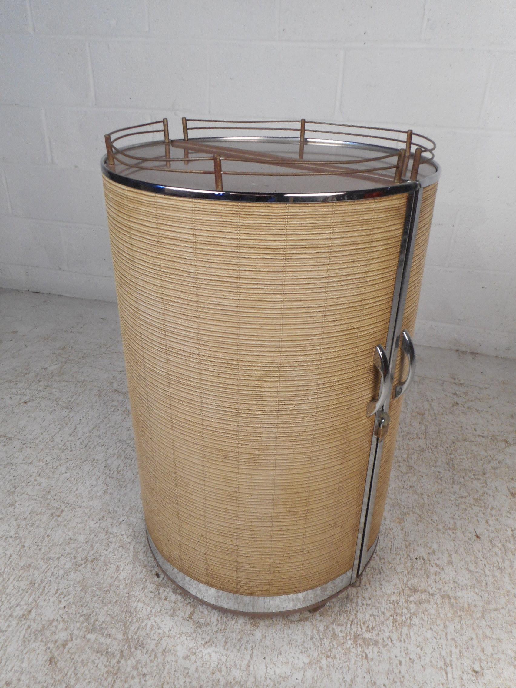 An interesting and unusual metal bar made by Semrow Products. This piece features a cylindrical body that opens to show a folding shelf and storage areas for bar accessories/bottles. The exterior features a beige lining with chrome trim on the base.