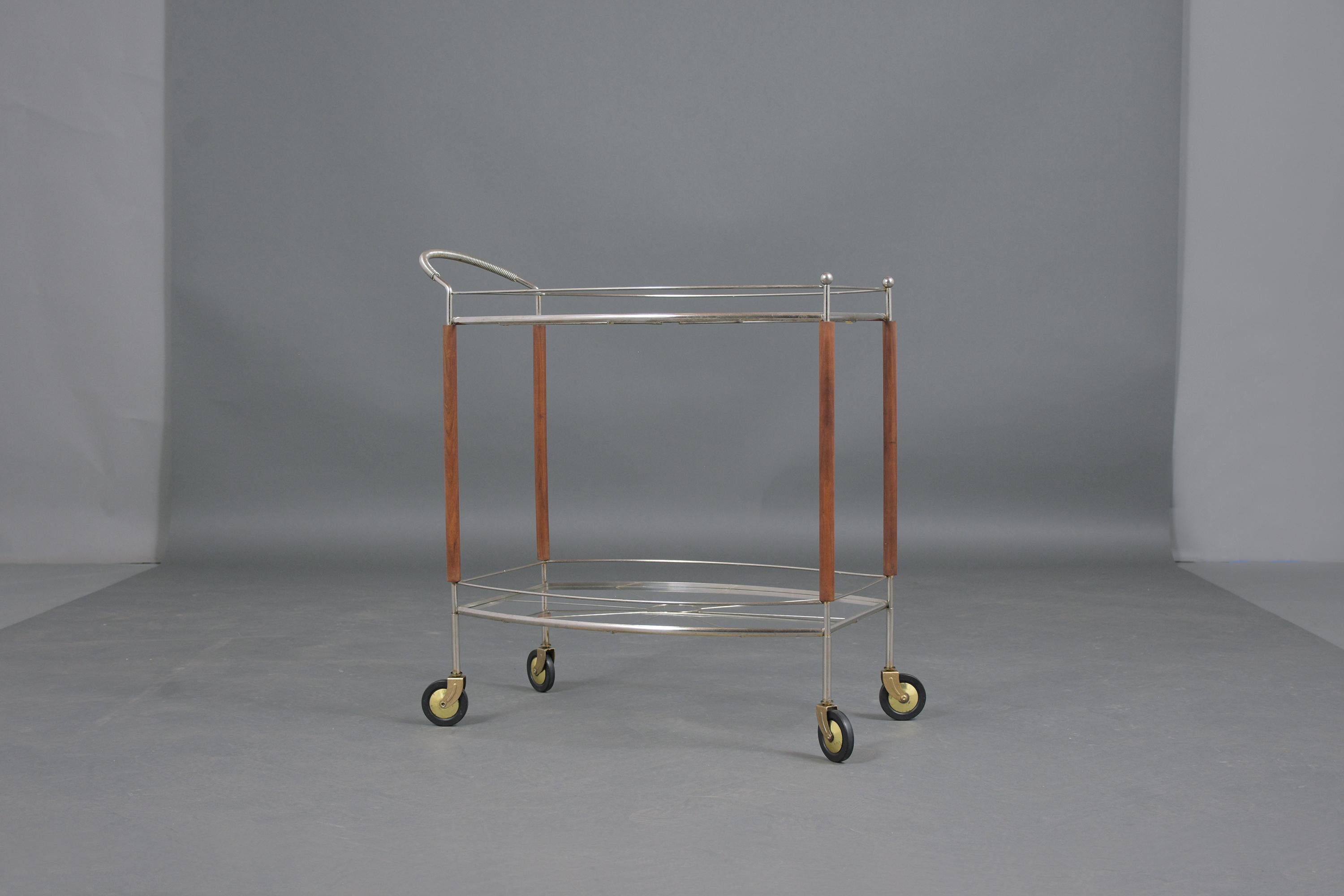 An extraordinary mid-century rolling bar cart that's beautifully crafted out of steel in great condition and ready to be used. The sturdy metal frame is chrome plated, comes with two glass shelves, and rests on its four original caster wheels with