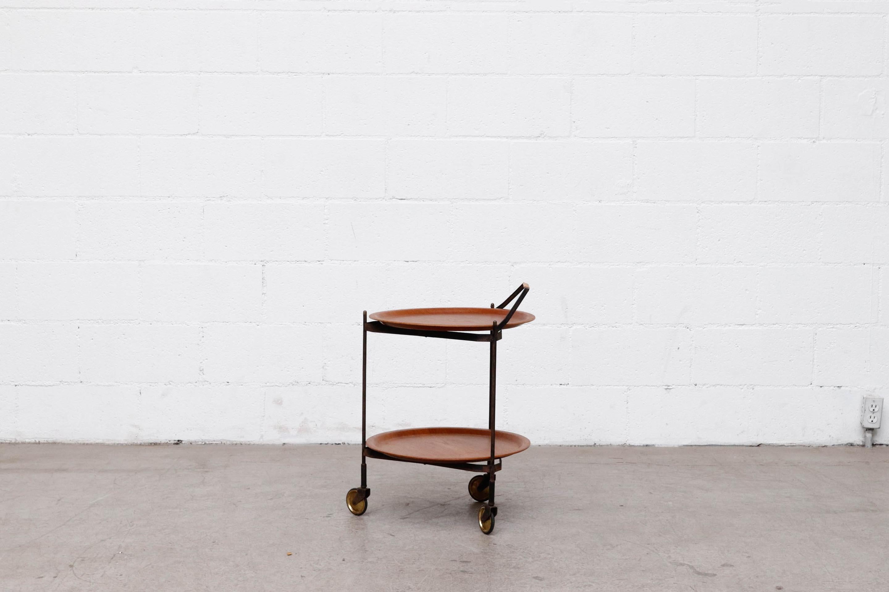 Awesome mid-century rolling cart with removable teak trays on folding black enameled metal frame with wheels and faux leather wrapped handle. Frame folds flat, trays can be removed. In original condition with lightly refinished trays and visible