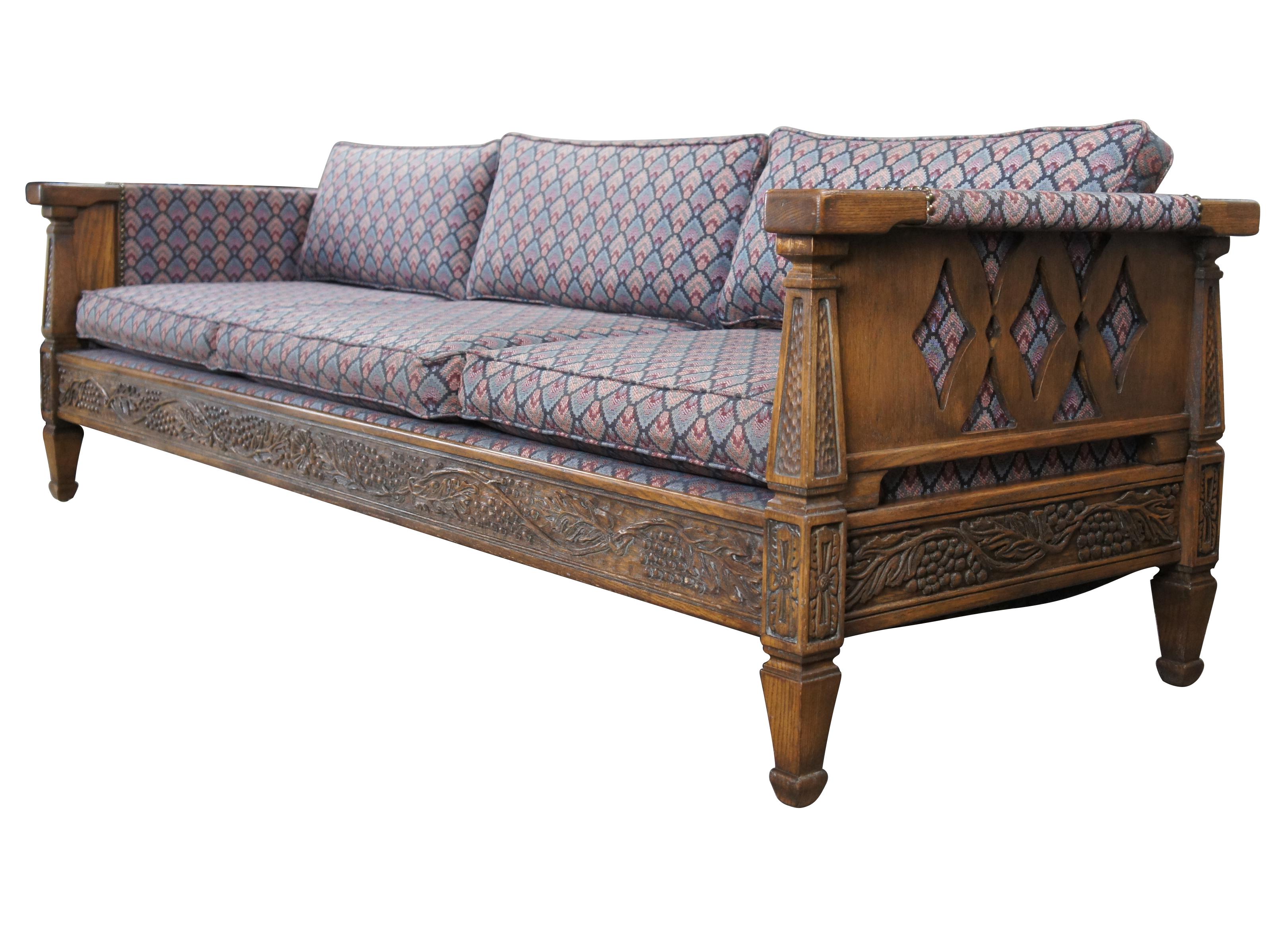 Romweber (R-13490) Viking oak three seat sofa / couch, circa 1984. Features rectangular carved oak frame with grapevine motif, tooled pillars and floral embellishments. Upholstered in a retro fan pattern with nail head trim along the arms. Outer