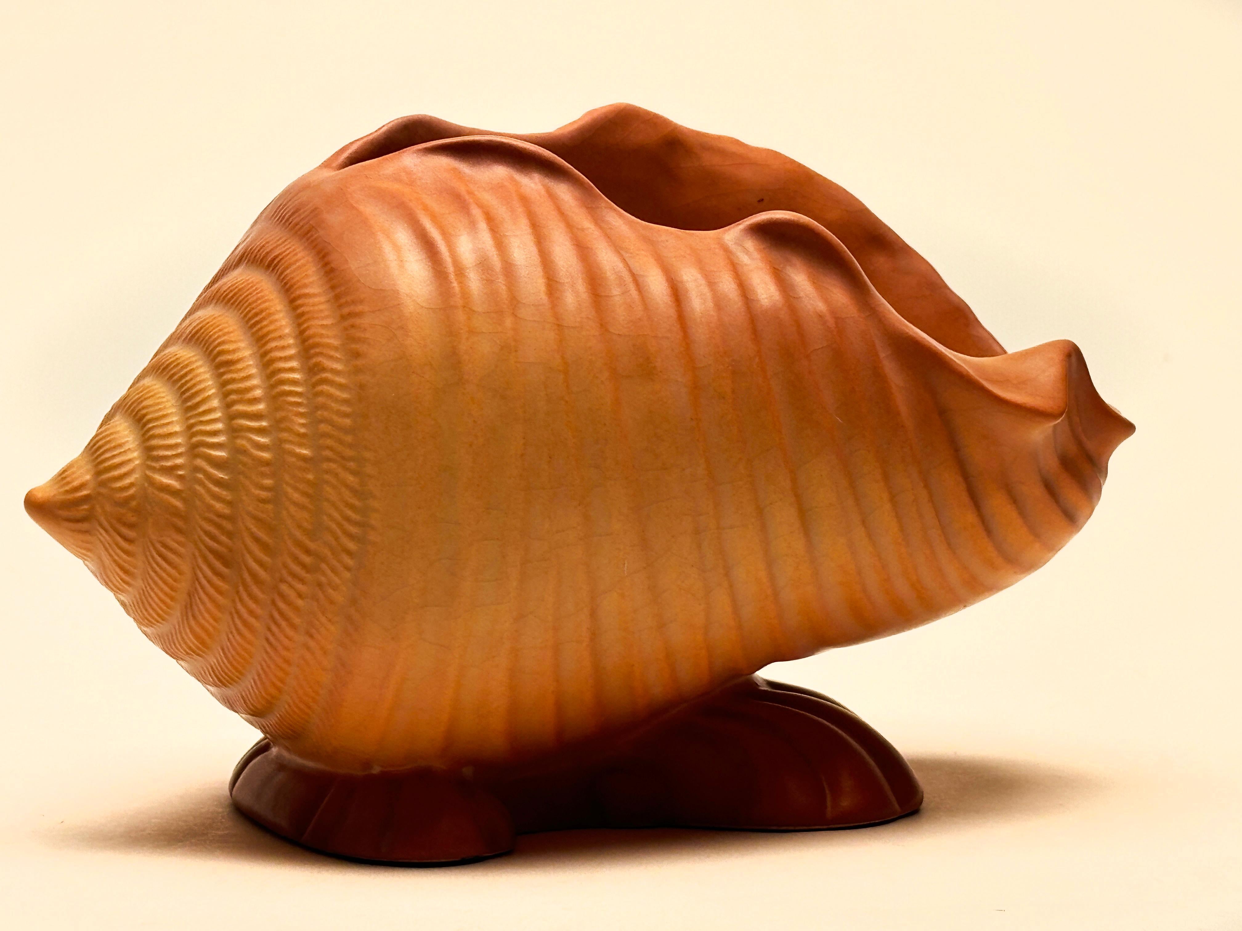 This rare terra cotta colored conch shell planter by Roseville Pottery is a stunning example of the beautiful soft mixture of terra cotta and peach shades covering a conch shell design that reflects a contemporary flair. This planter was made
