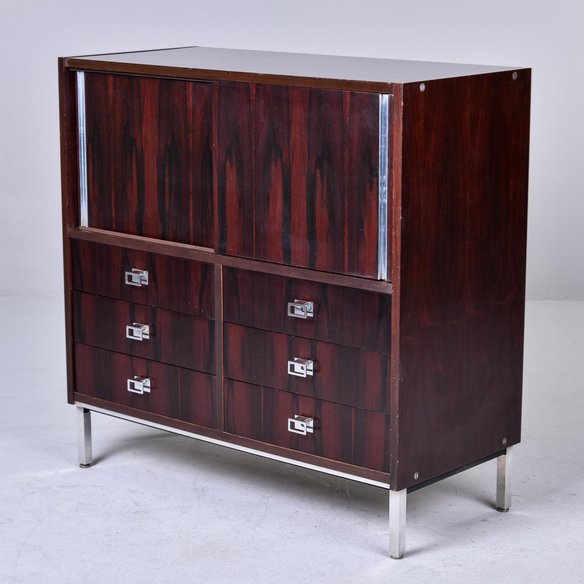 Found in Italy, this circa 1960s cabinet by Mim of Italy has a chrome base and legs supporting a rosewood cabinet. Cabinet consists of wood with rosewood veneer. Top section of cabinet has two sliding doors that open to a storage compartment. Bottom