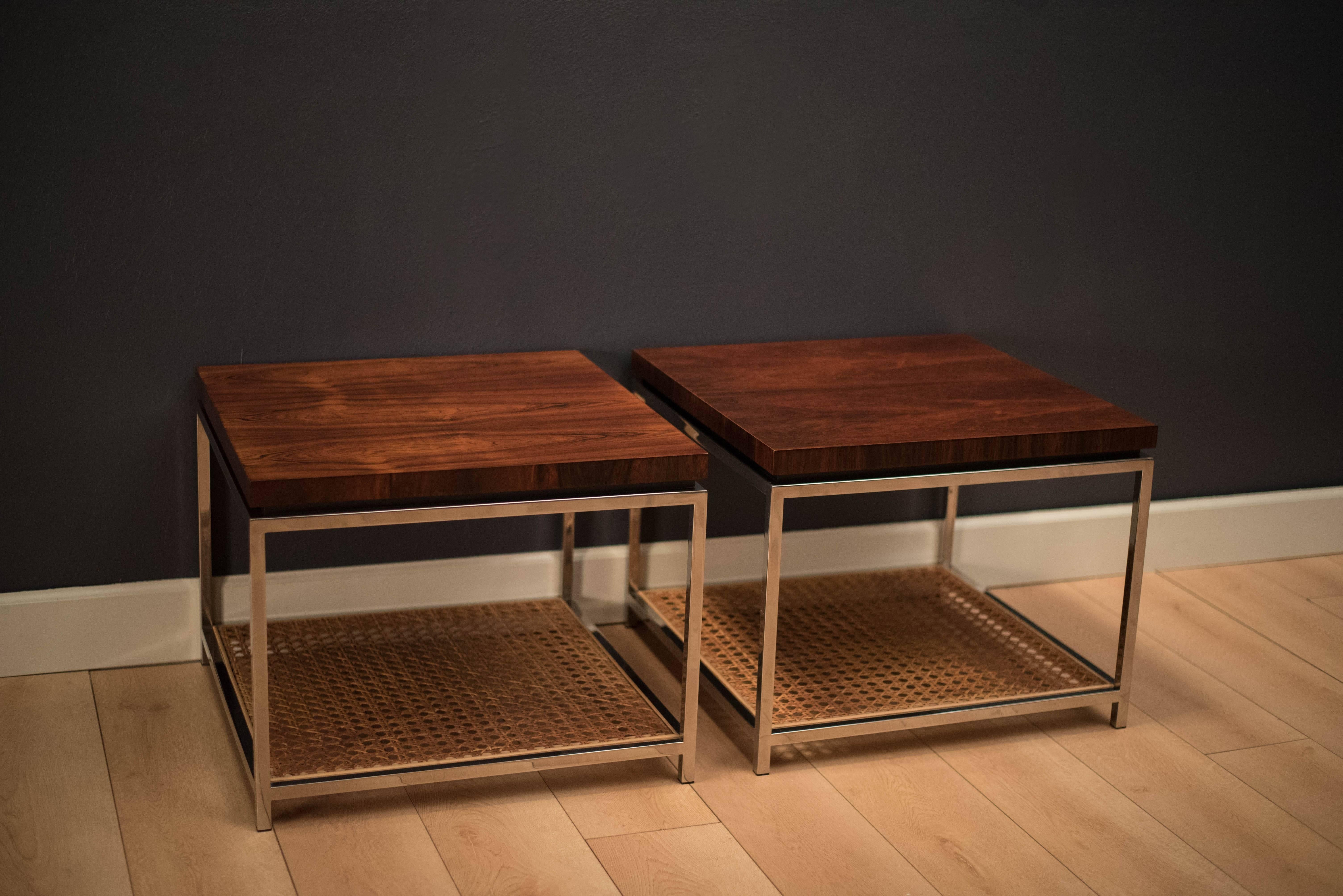 Mid-century modern pair of square side tables in rosewood and chrome. Each table includes a lower tiered rattan shelf. Continuous rosewood grain is displayed at every angle.