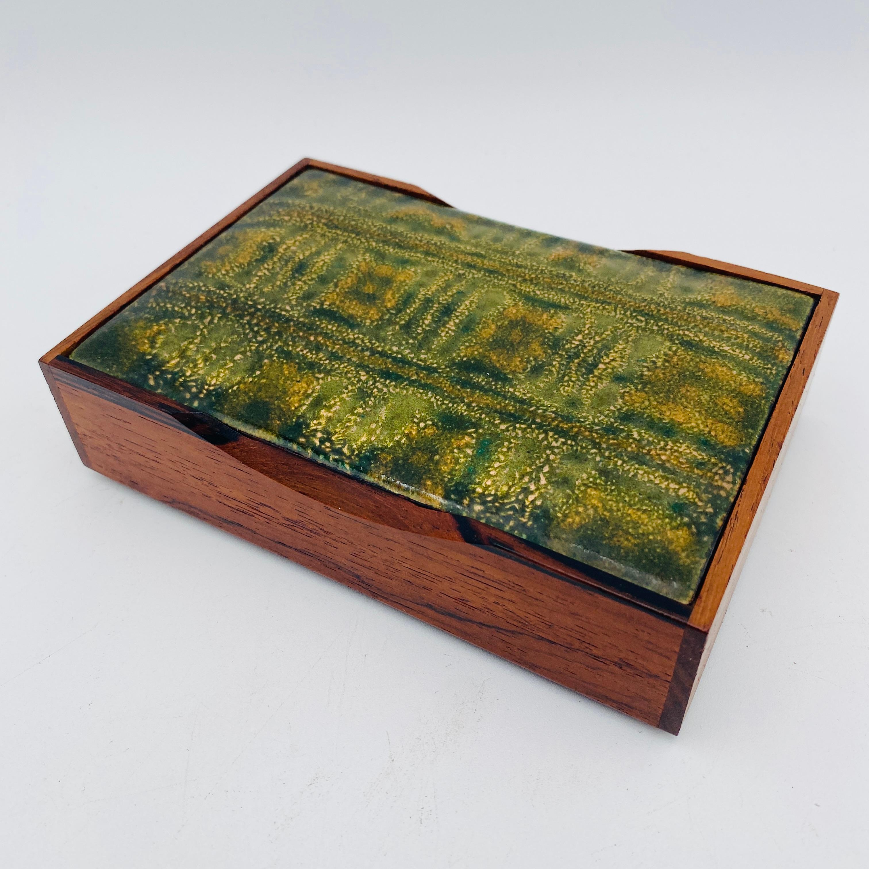 Il s'agit d'une superbe boîte en bois rouge avec un couvercle en émail. Il est à la fois décoratif et fonctionnel puisqu'il permet de ranger des bijoux ou tout autre objet de votre choix. Non signée. 
