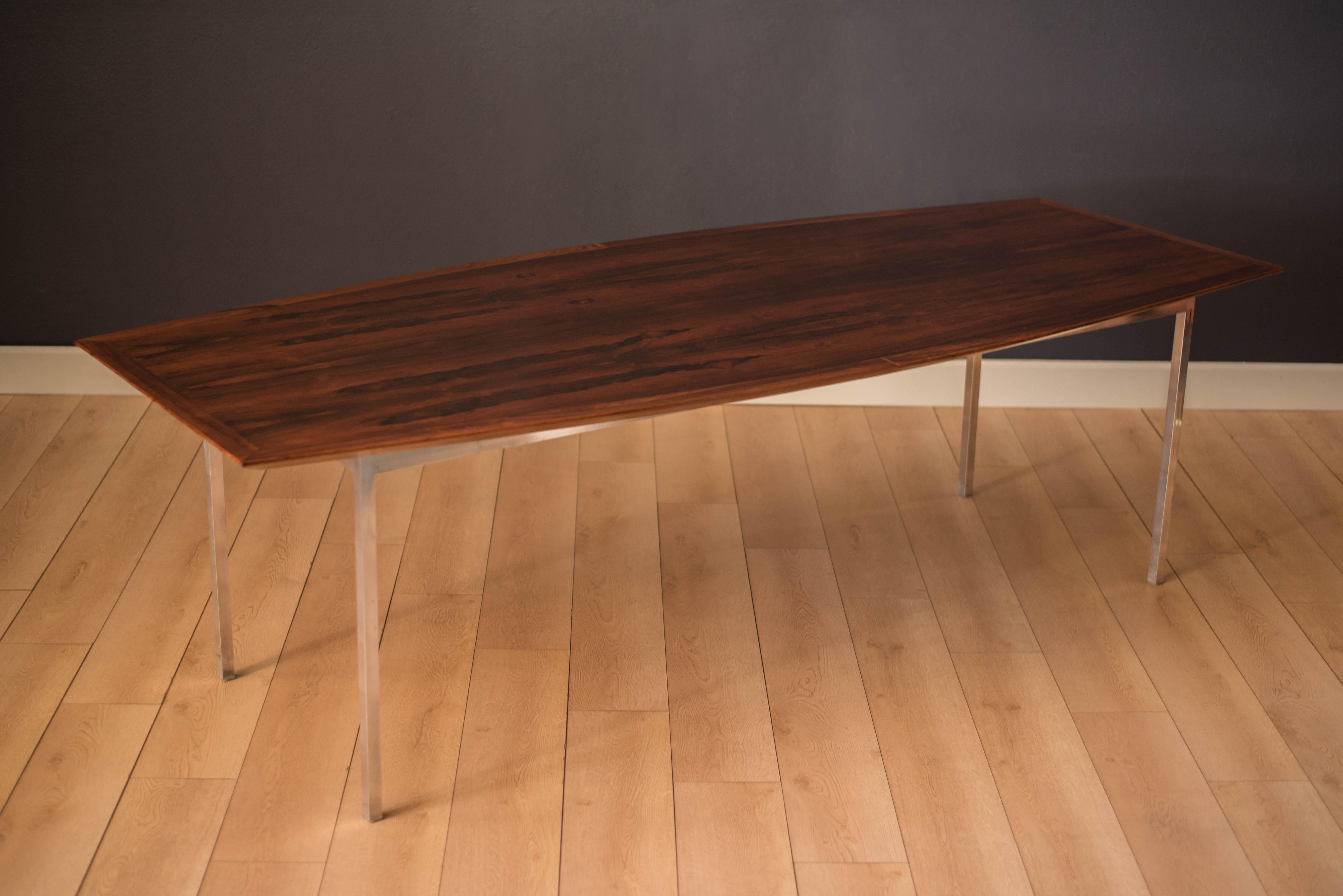 Vintage dining or conference table in Brazilian rosewood designed by Florence Knoll. This piece features a boat shaped tabletop supported by a rectangular steel base finished in polished chrome. Perfect for large gatherings and becomes a focal point