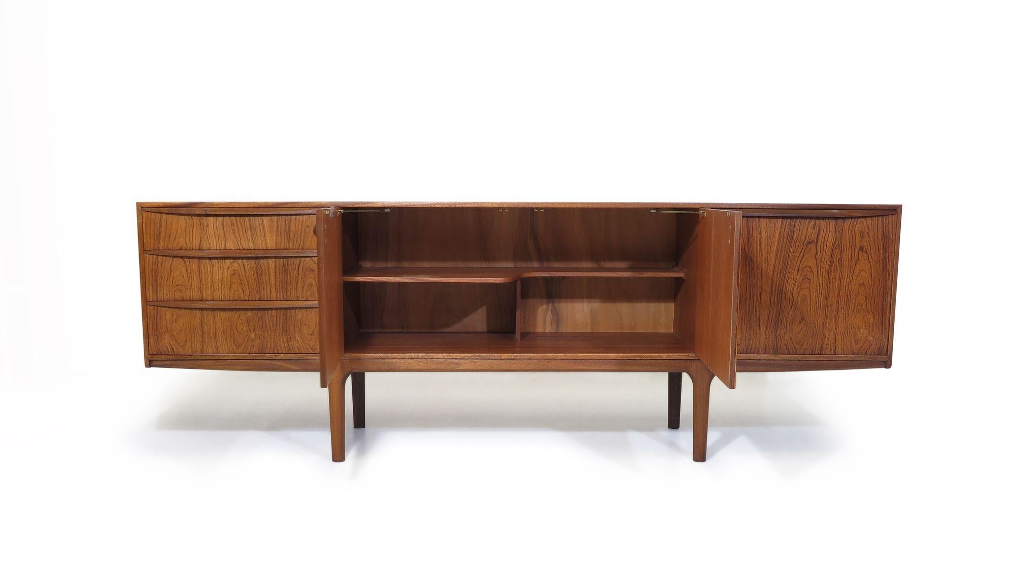 Mid Century rosewood credenza crafted of faded rosewood with three drawers on left, pair of cabinet doors in center for bottle storage, and drop-front cabinet on right. Glass top. The credenza has original finish, good condition with signs of age