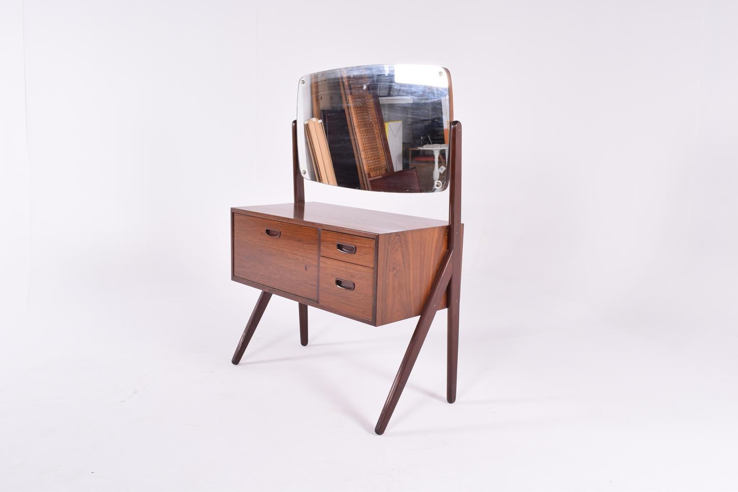 Danish dressing table made in rosewood from the 1960s. The model has two drawers an and one compartment with door. A large tiltable mirror and is standing on a nicely designed base in teak.