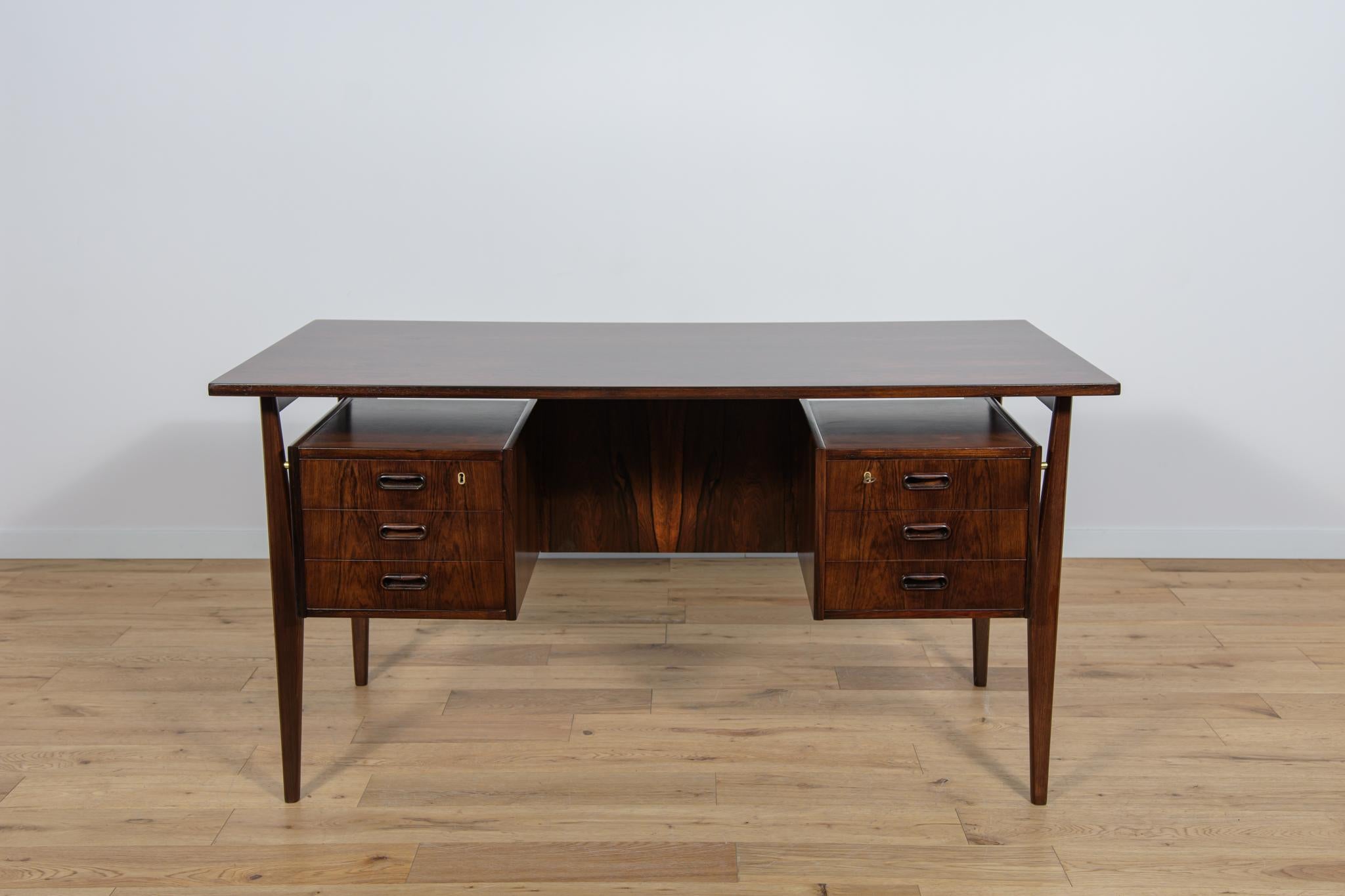 The desk designed by G. Nielsen Tibergaard was produced in Denmark in the 1960s. The desk is made of rosewood and free standing thanks to the finished back side with open storage space for books. On the front there are two drawer modules with three