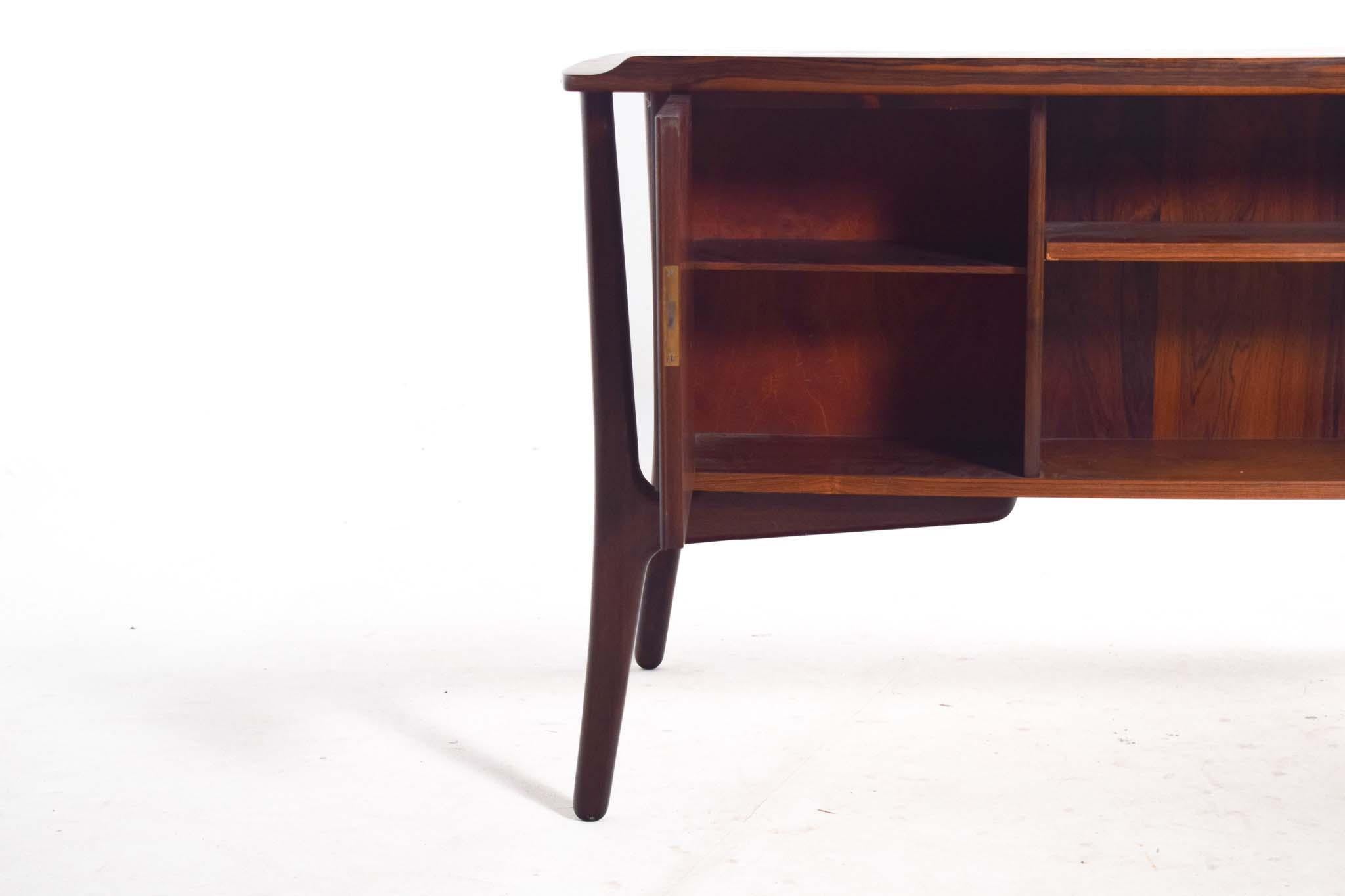This Mid-Century Modern rosewood desk, designed by Svend Aage Madsen for Sigurd Hansen, exudes timeless elegance and exceptional craftsmanship. The desk's sculptural silhouette features smooth, curved edges and striking details, including six