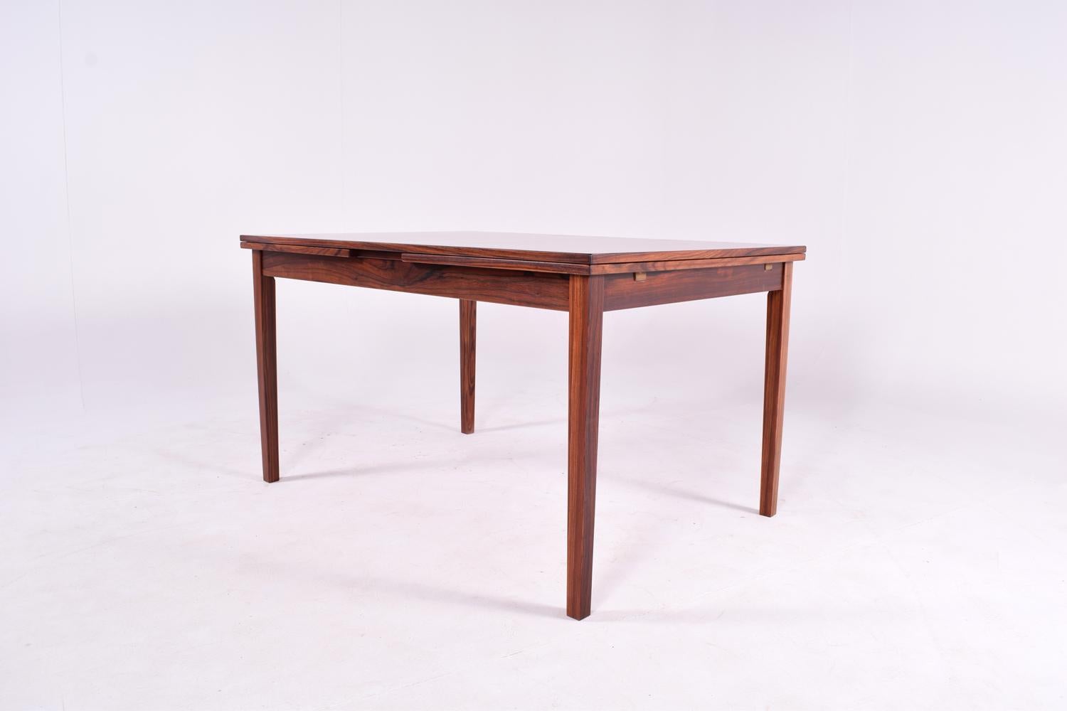 Midcentury Danish dining table designed by Kaj Winding, an amazing table with beautiful rosewood veneer, elegant geometric design and great craftsmanship.
A rosewood frame circles the top of the table and of the two leaves, creating a pattern when