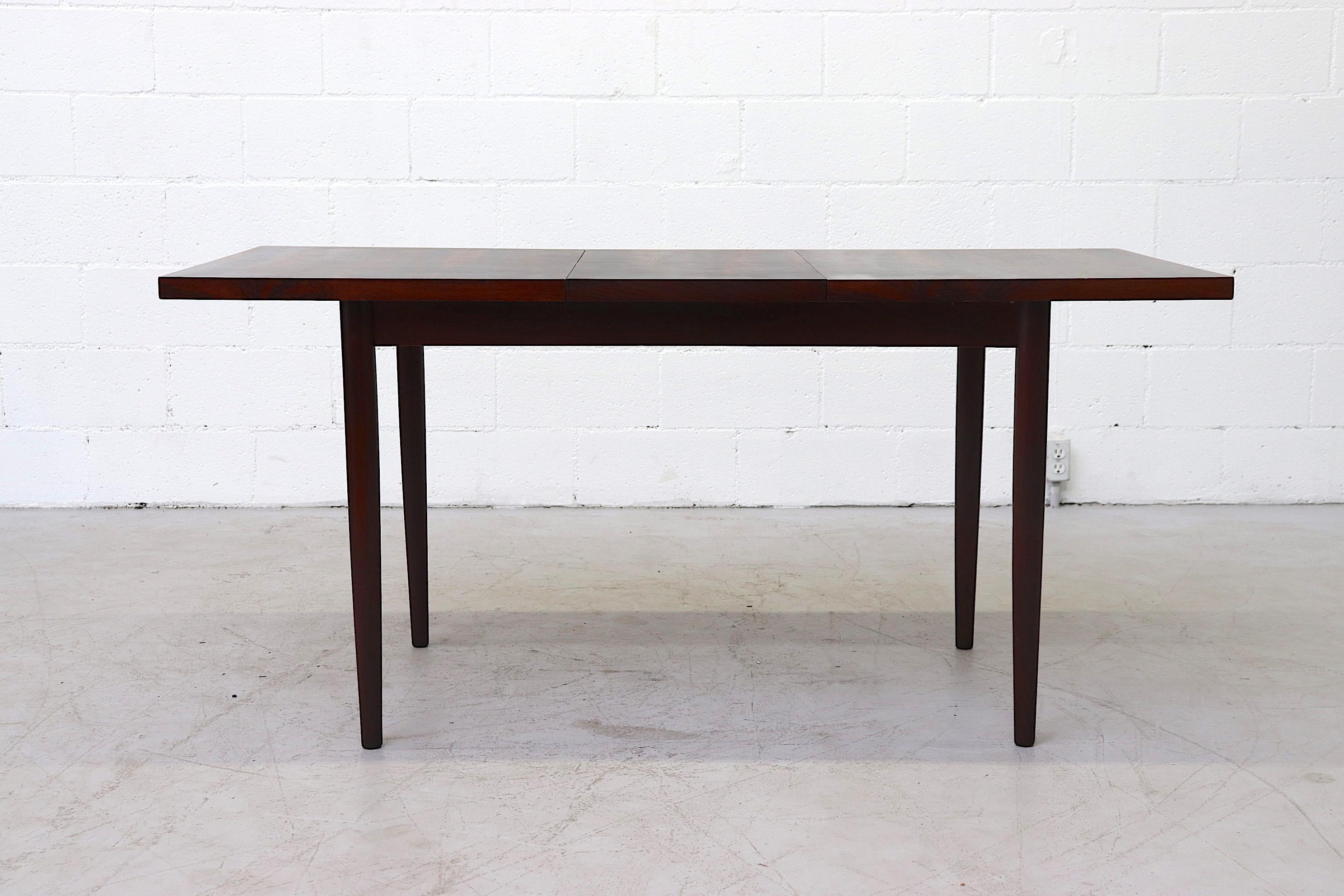 Beautiful rosewood dining table with hidden leaf and lightly refinished with round wood legs. In original condition with wear consistent with age. Table extends to 62.5
