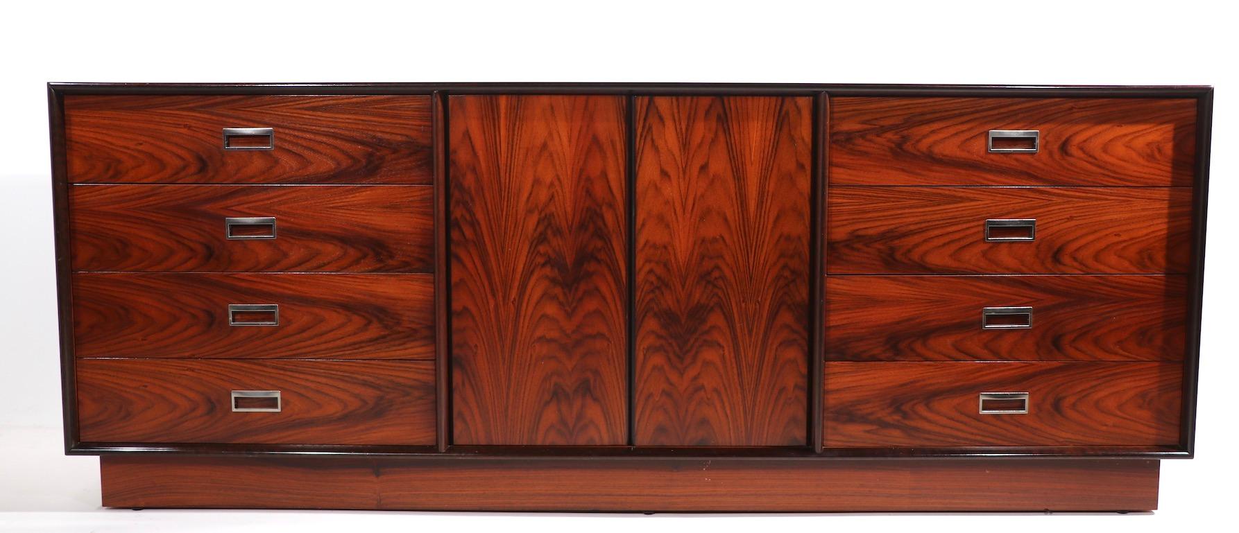 Stunning rosewood dresser, credenza in very fine original condition. The dresser has two banks of 4 drawers, which flank a two door storage space. The chest is on a plinth base, and has chrome trim handles. Rich, vibrant veneer creates impressive