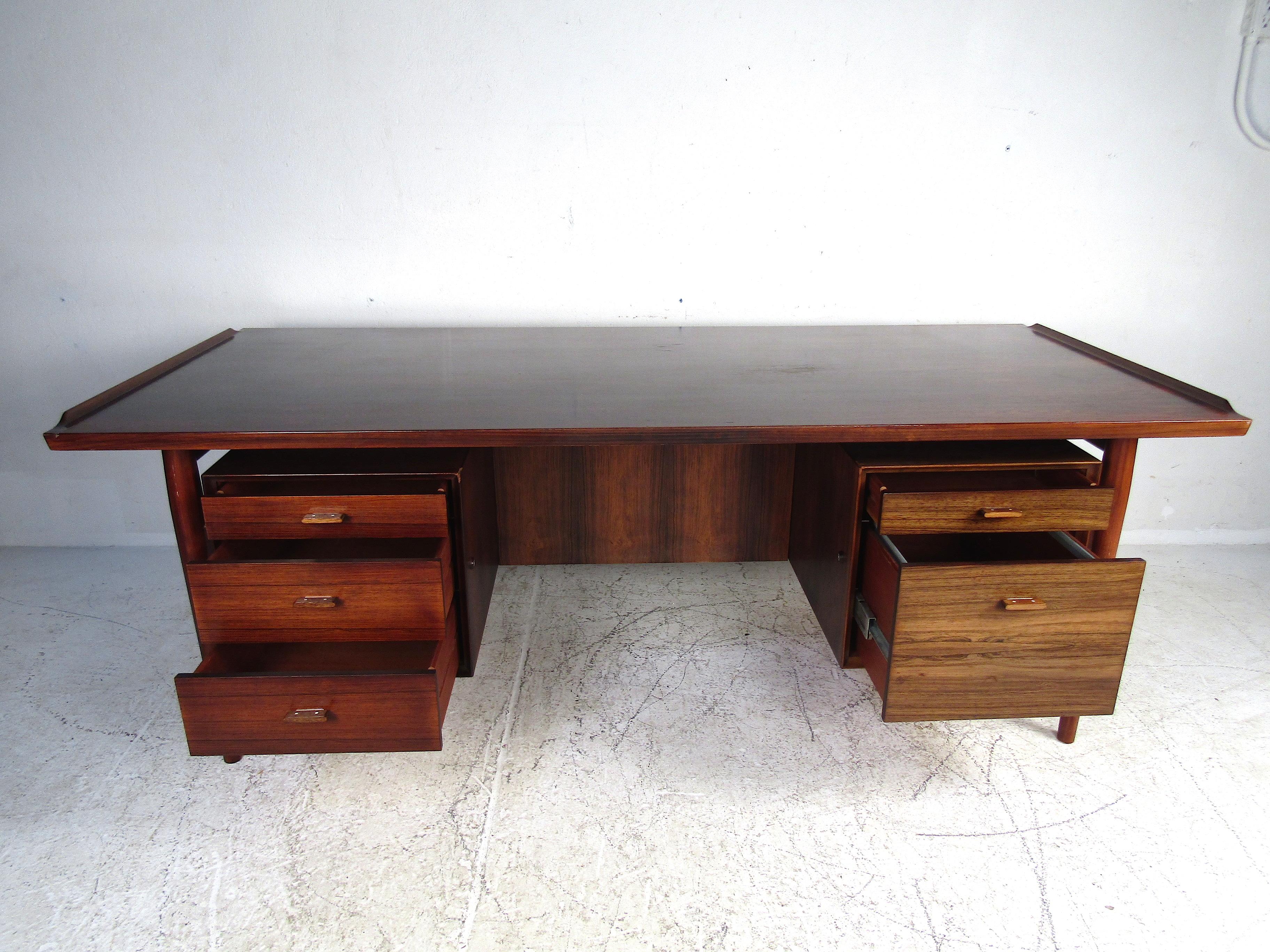 Stunning midcentury executive desk with a rosewood veneer and finished back. Large table surface with raised accents on either end. Spacious drawers and a filing cabinet flanking the piece. Great piece sure to impress in any home, business, or