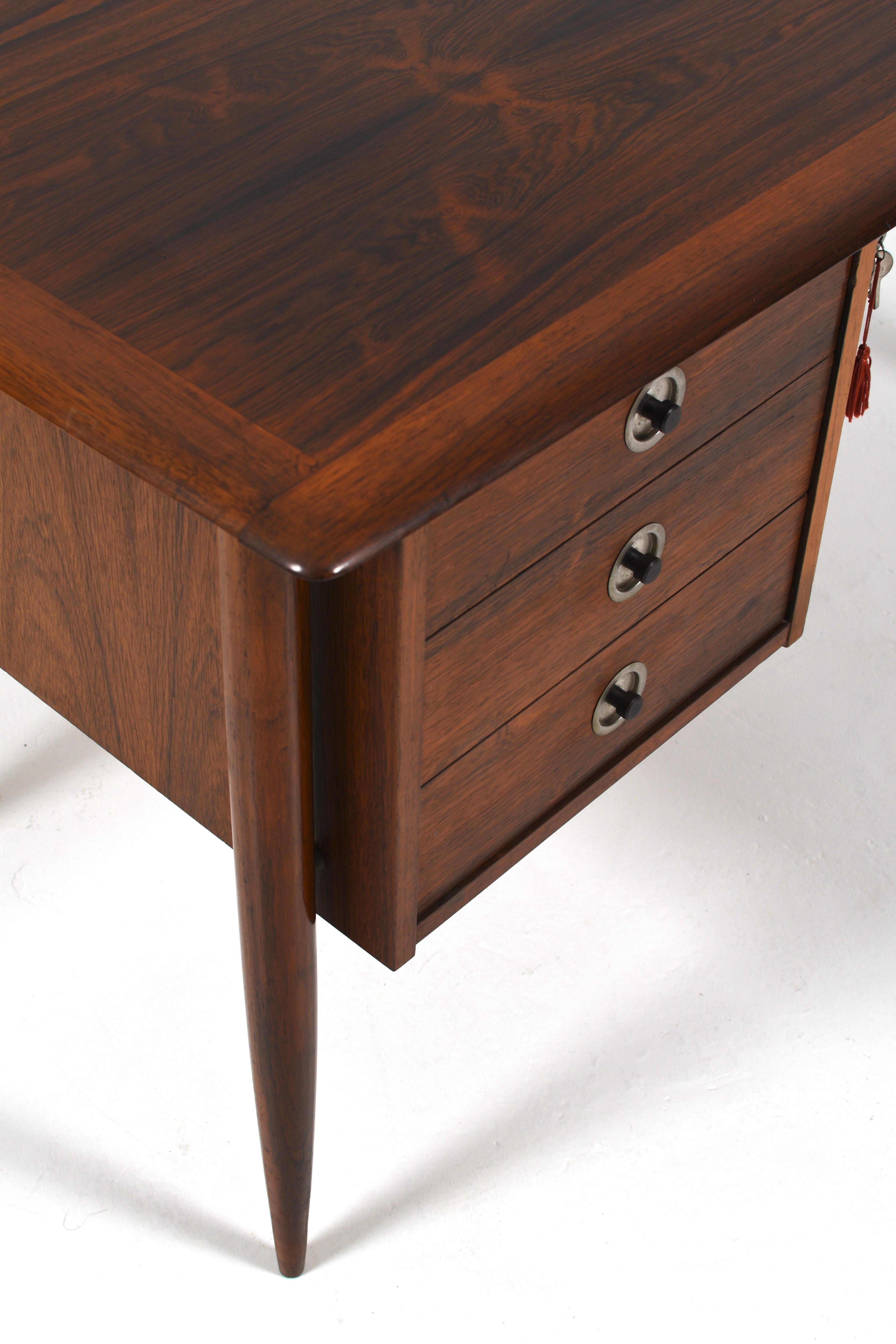 Straordinaria scrivania direzionale della metà del secolo scorso realizzata in legno di palissandro riccamente venato, risalente agli anni Sessanta. Questo pezzo di modernariato scandinavo è caratterizzato da eleganti gambe affusolate, un piano