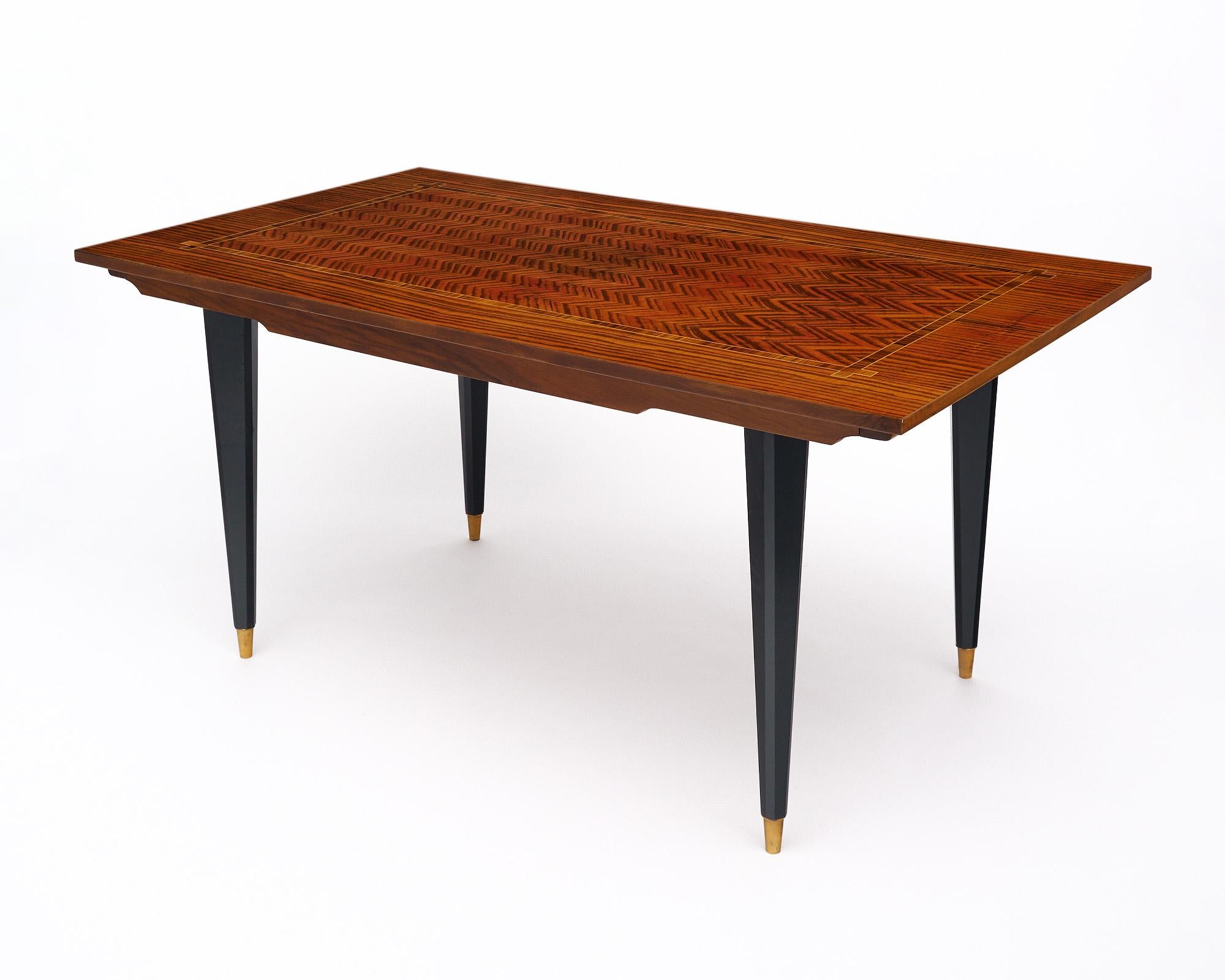 Mesa de comedor de mediados de siglo en Francia fabricada con un hermoso tablero chapado en palisandro. Tiene una llamativa encimera de parquet con un dibujo de chevron. El diseño está perfilado con una incrustación de madera de limón. El delantal