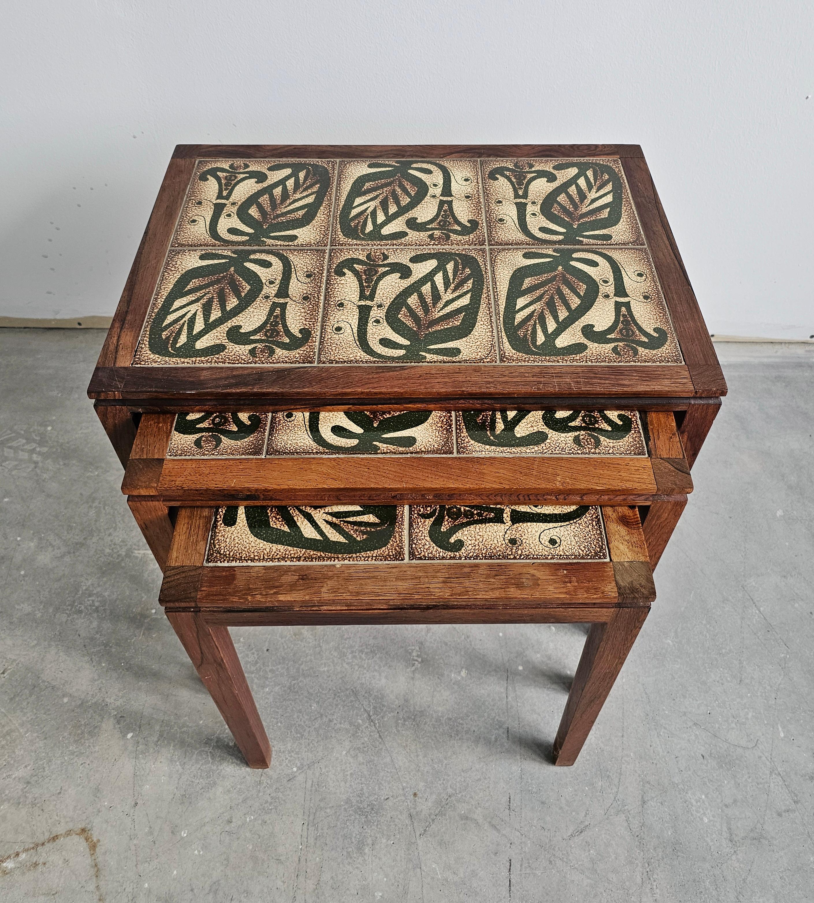 Mid Century Modern set of nesting tables, with tiles on top. Wooden frames are done in solid rosewood, also known as palisander. This set was made in Denmark (1960s). Manufacturer's stamp is visible on the bottom of each table, but very pale and