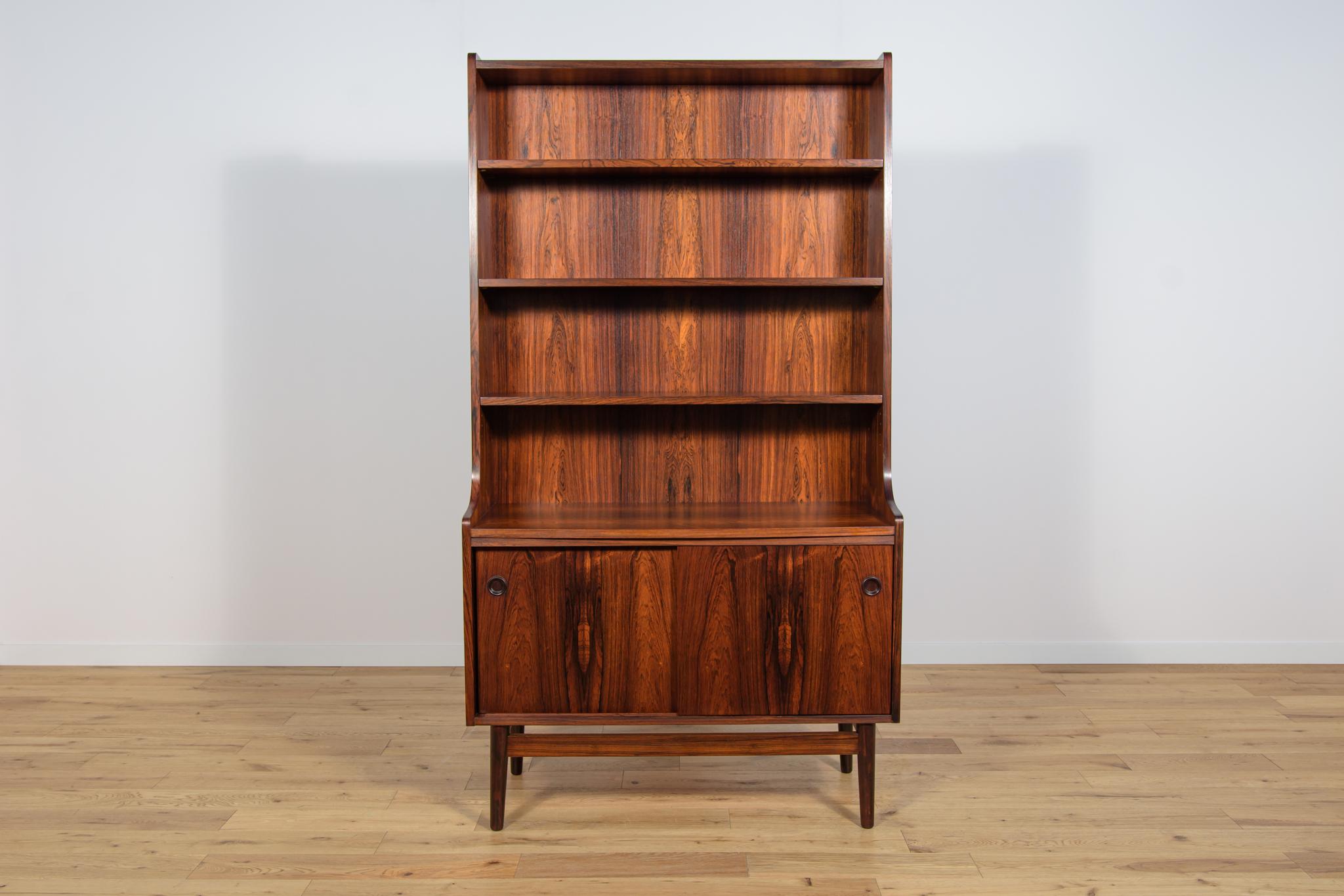 This Mid-Century Danish designed shelf was designed by Johannes Sorth and manufactured by Bornholms Møbelfabrik. It is made of rosewood. In the upper part of the bookcase there are four shelves, in the bottom part there are a sliding door cabinet.