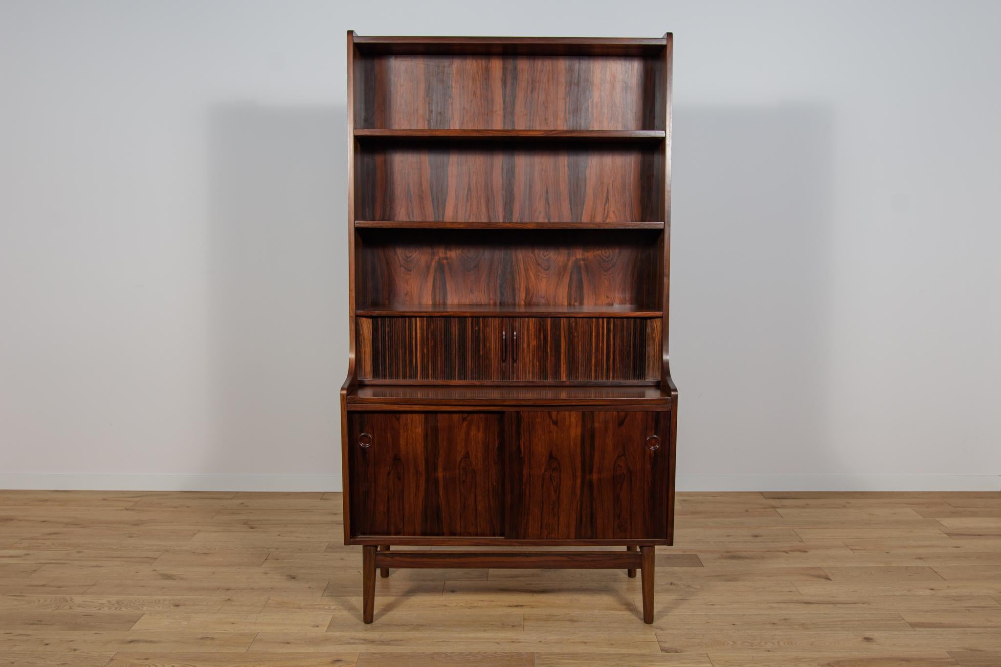 This Mid-Century Danish designed shelf was designed by Johannes Sorth and manufactured by Bornholms Møbelfabrik. It is made of rosewood. In the upper part of the shelf there are open three shelves, below there is a module with three small drawers