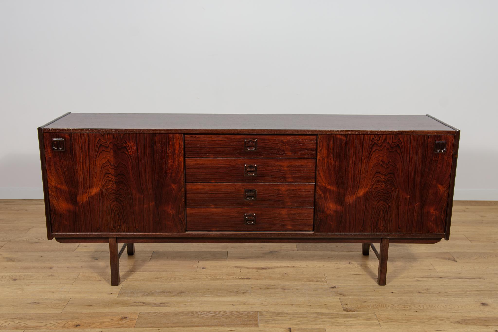 La credenza fu disegnata da Erik Wortz per la fabbrica svedese Ikea negli anni '60. La credenza è realizzata in legno di palissandro e presenta maniglie profilate. Ha quattro cassetti al centro e due ante scorrevoli. È stata sottoposta a una