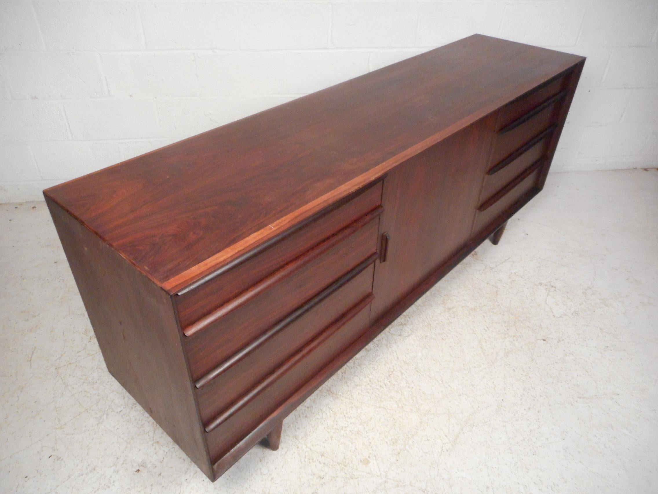 Impressive midcentury sideboard with a beautiful rosewood construction with a dark finish. Ample storage space, with compartments within allowing for sorting and filing of drawer's contents. A finished back allows this sideboard/server to be