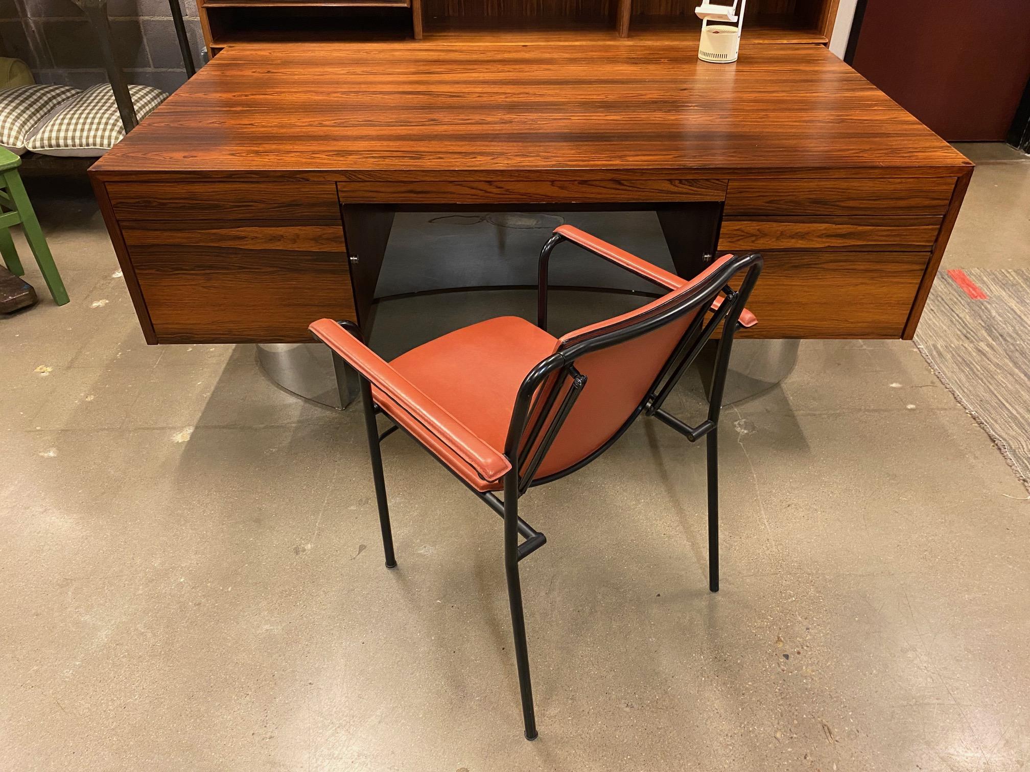 Mid-century rosewood veneer and stainless steel executive desk.  Six drawer kneehole desk is constructed of active grain Brazilian rosewood which rests on a mirror polished stainless steel crescent shape base.  Single full depth file drawer plus